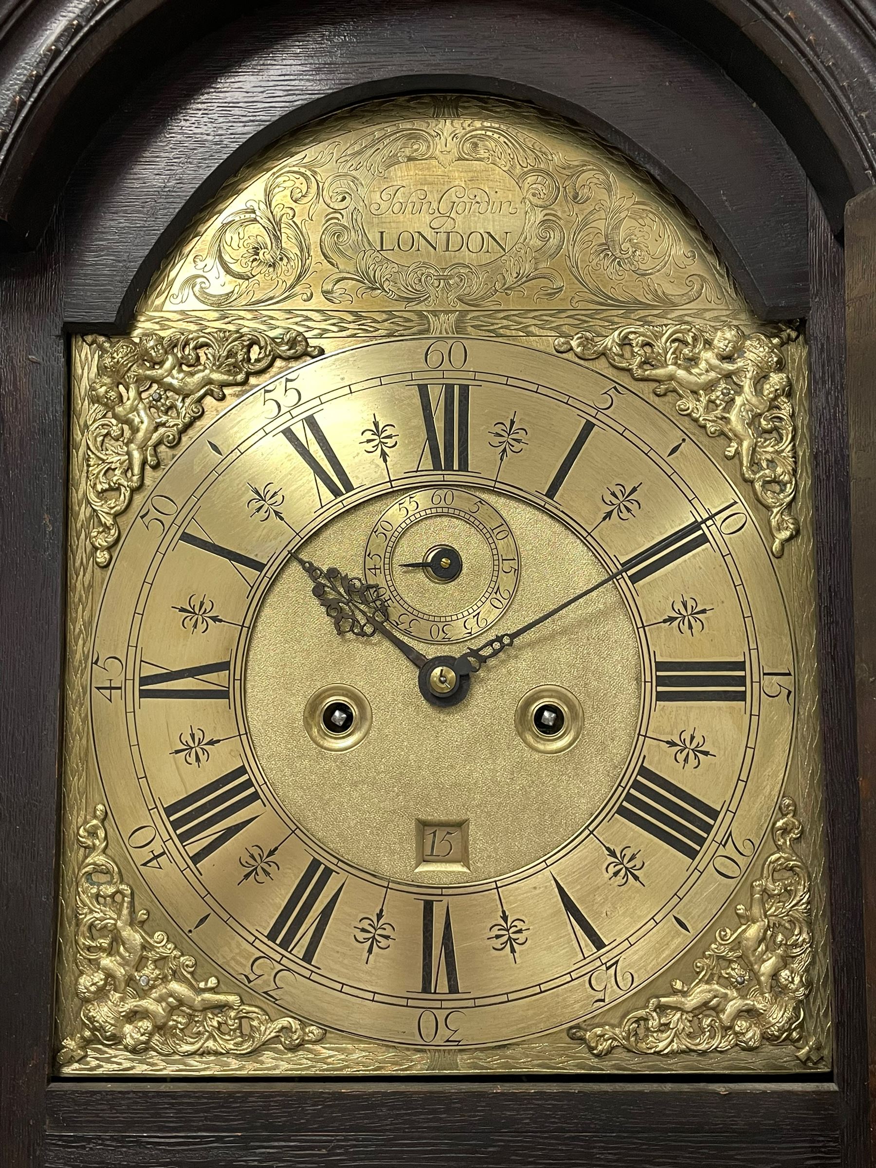 18th-century profusely carved oak longcase clock - with a pagoda pediment, upstands and carving, 
 break arch hood door flanked by reeded pilasters with brass capitals, trunk with canted corners and a spire topped door, square plinth with applied skirting, break arch brass dial with wheatsheaf engraving and cast cherub and crown spandrels, engraved break arch with the London clockmakers name John Gordin, silvered chapter ring with Roman numerals, five minute Arabic's, minute and quarter hour tracks, matted dial centre with ringed winding holes, square date aperture and seconds ring, dial pinned to a five pillar movement with inside countwheel striking, striking the hours on a cast bell. With weights and pendulum. John Gordin, is possibly a mis-spelling or phonetic spelling of John Gordon, of London, who worked from Ludgate Street in the parish of St. Gregory by St. Pauls. Apprenticed in 1689 and died in 1732 when his will was proven.
