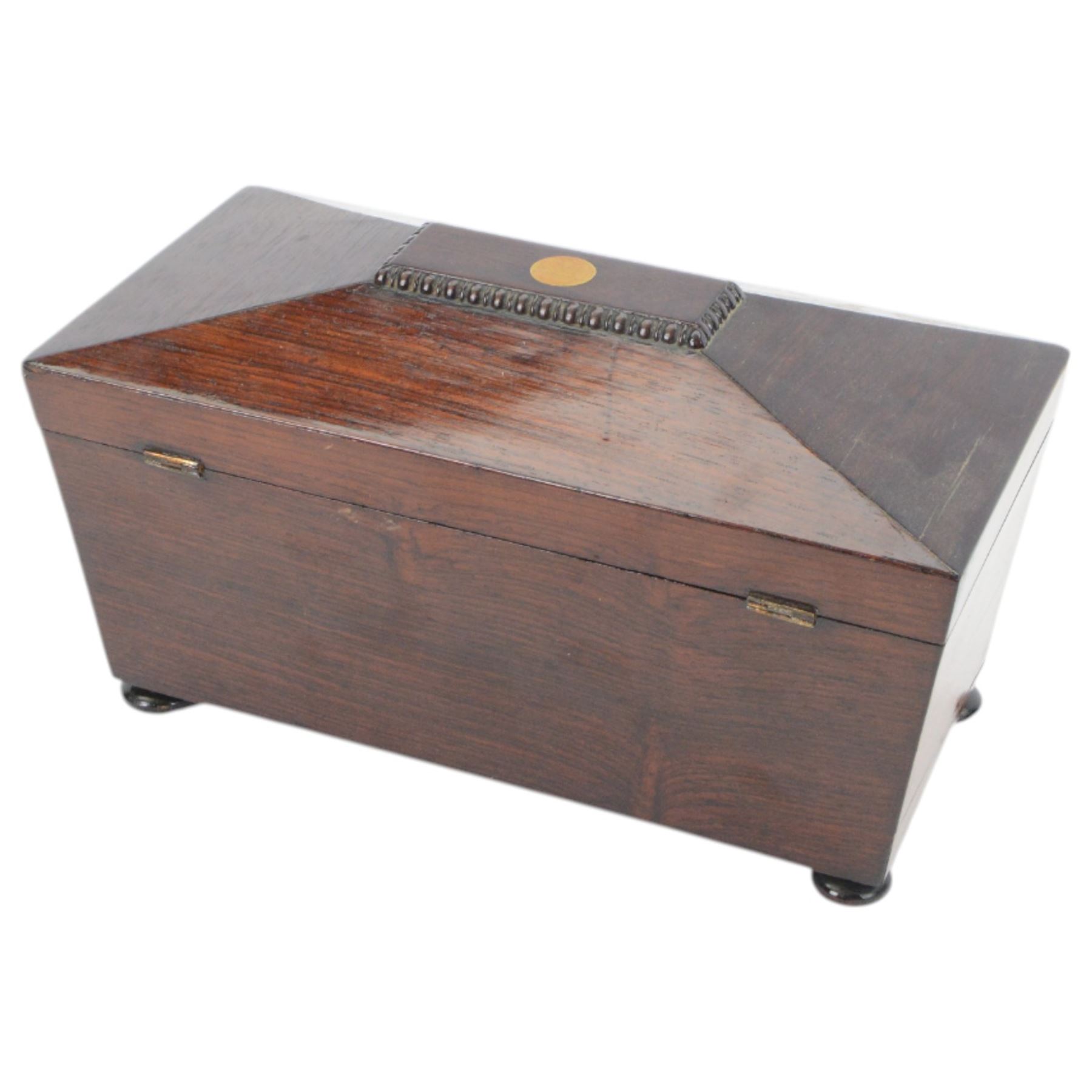 19th century rosewood sarcophagus shaped tea caddy, the hinged lid with brass cartouche to the centre, opening to reveal a fitted interior with central glass bowl flanked and lidded compartments to either side, upon squat bun feet, H17cm