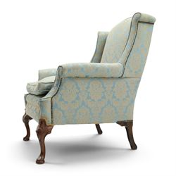 Georgian design carved mahogany framed wingback armchair, high wingback over sprung seat and loose cushion with rolled arms, upholstered in cyan ground gilt foliate damask fabric, on shell-carved cabriole supports with pad feet