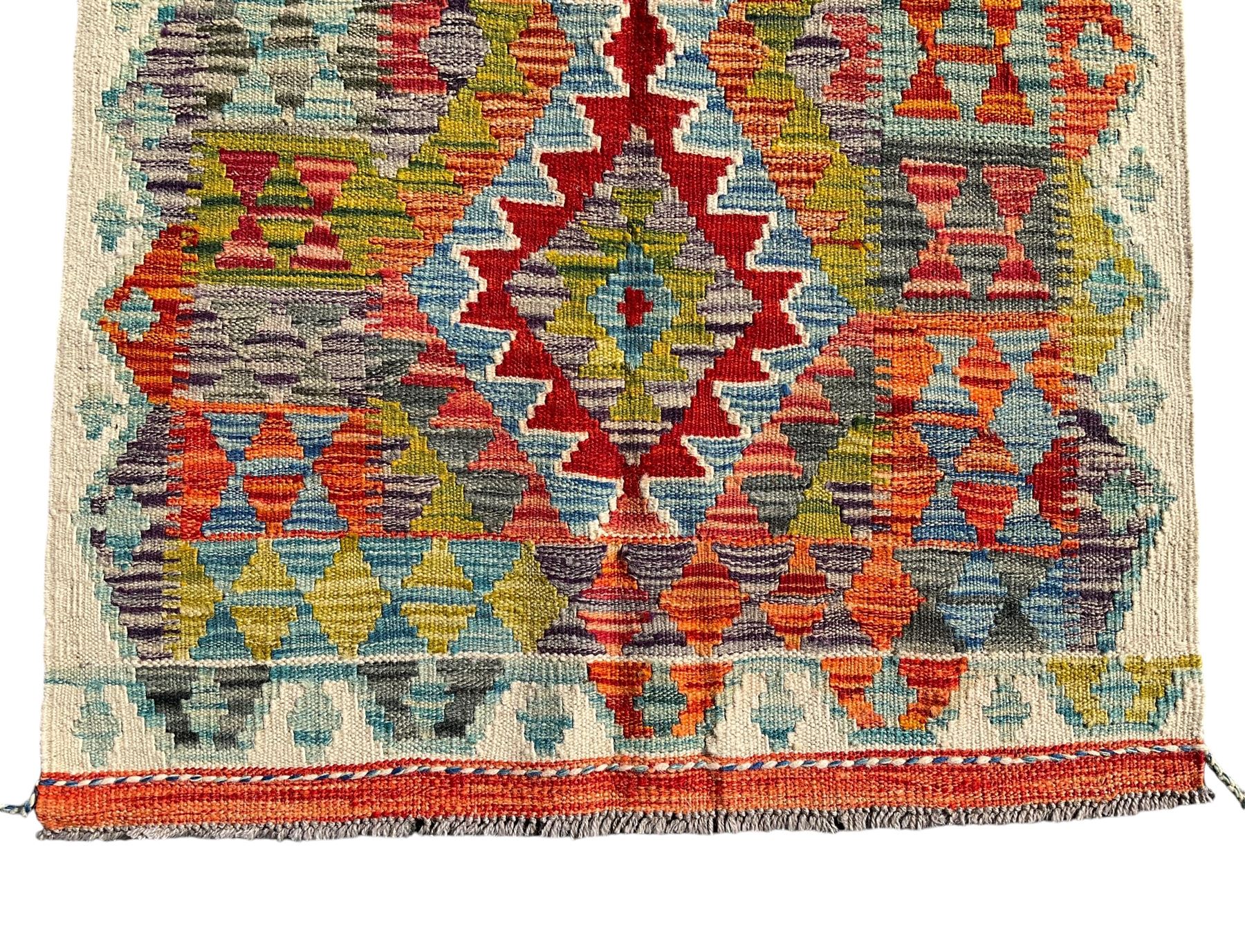 Afghan Chobi Kilim ivory ground rug, central geometric design consisting of stacked lozenge medallions in shades of red, green, and blue, flanked by multicoloured triangular motifs, guarded by zigzag patterns in contrasting tones