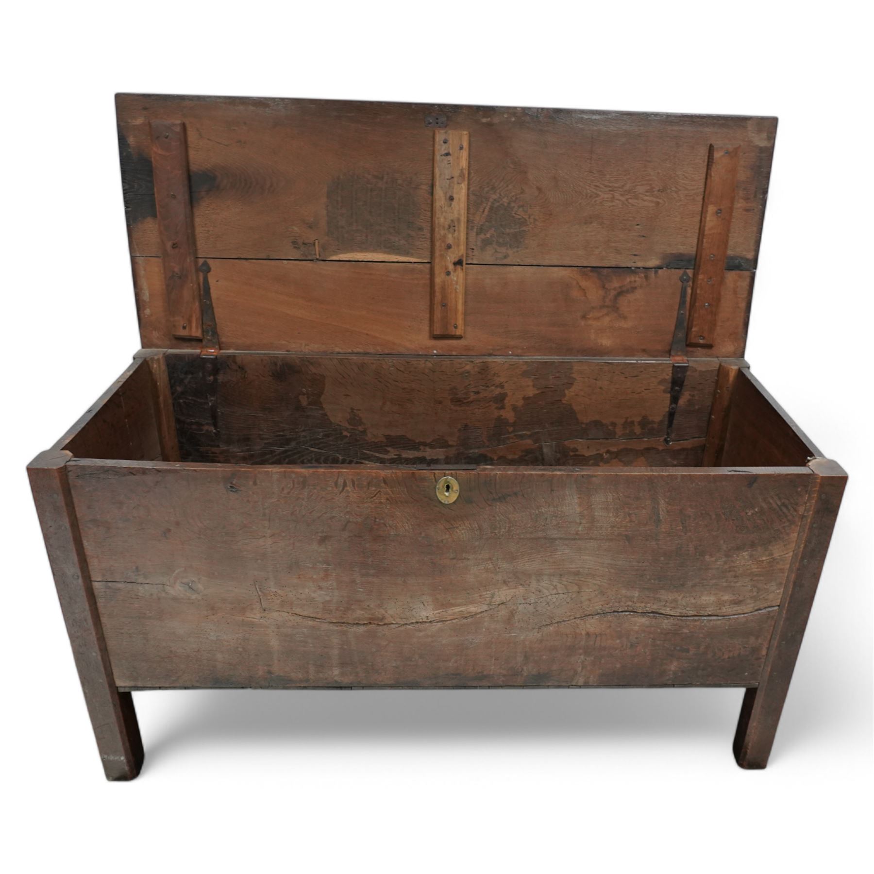 Large late 17th Century oak coffer, the hinged lid with twin rear strap hinges above a plain front with inset brass escutcheon, raised on square supports with pegged joinery and displaying pronounced grain figuring to the single front board
