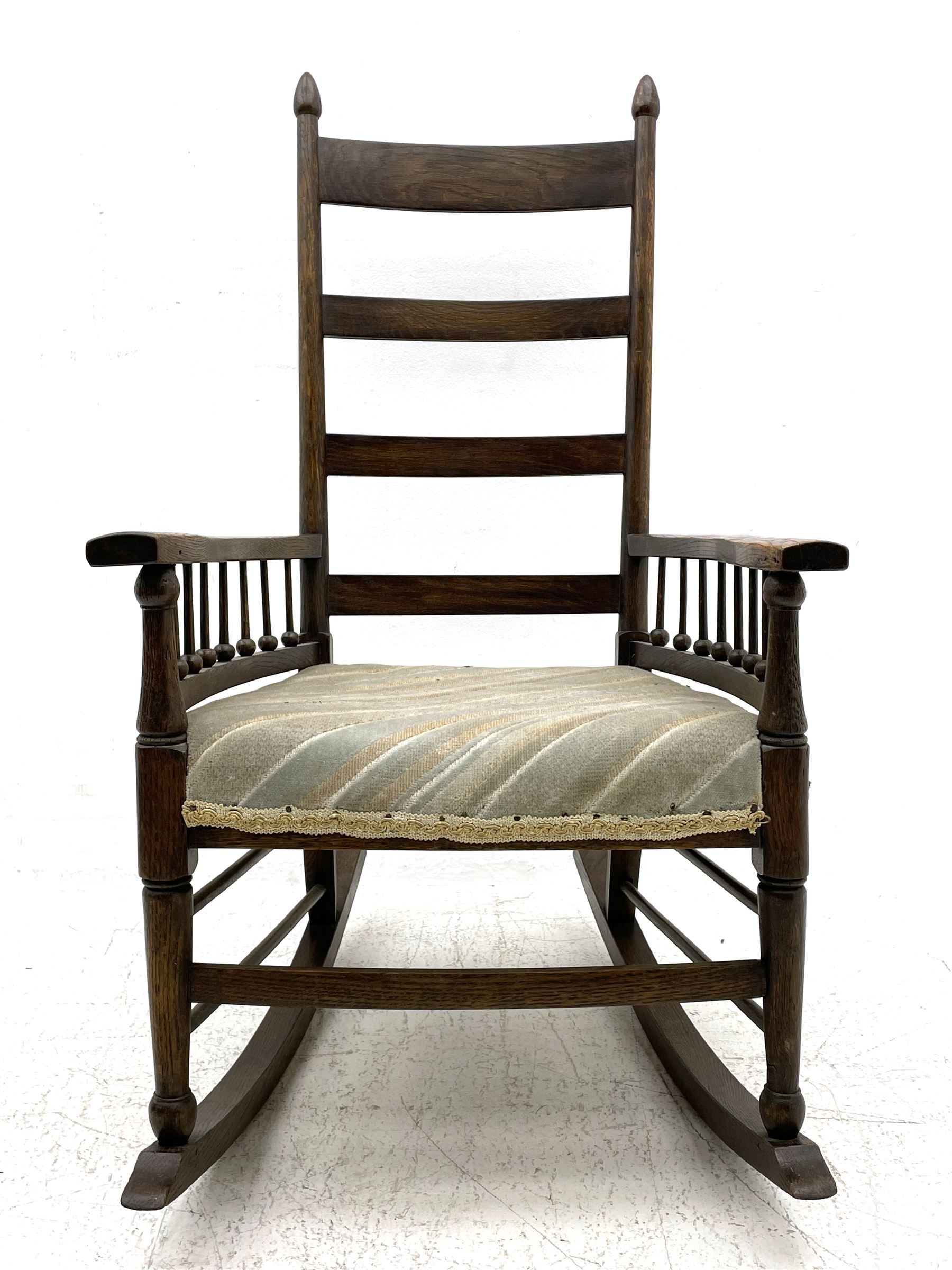 William Birch for Liberty & Co. - Arts and Crafts period oak ladder back rocking chair, the arms supported by a series of turned spindles, upholstered seat