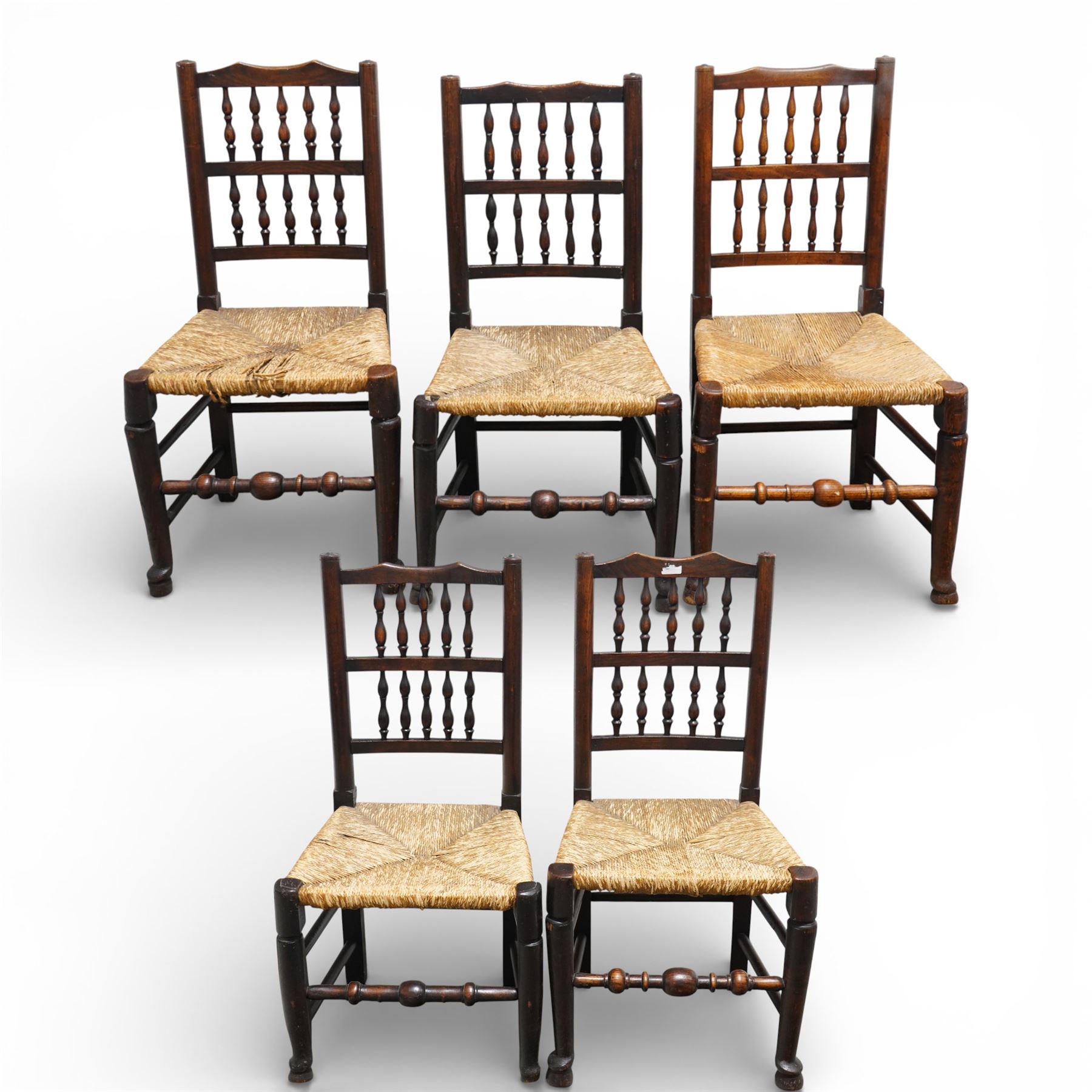 Set of five 19th century elm spindle back chairs, with shaped crest rails above double rows of turned spindles, rush seats, turned legs joined by stretchers supported on turned pad feet