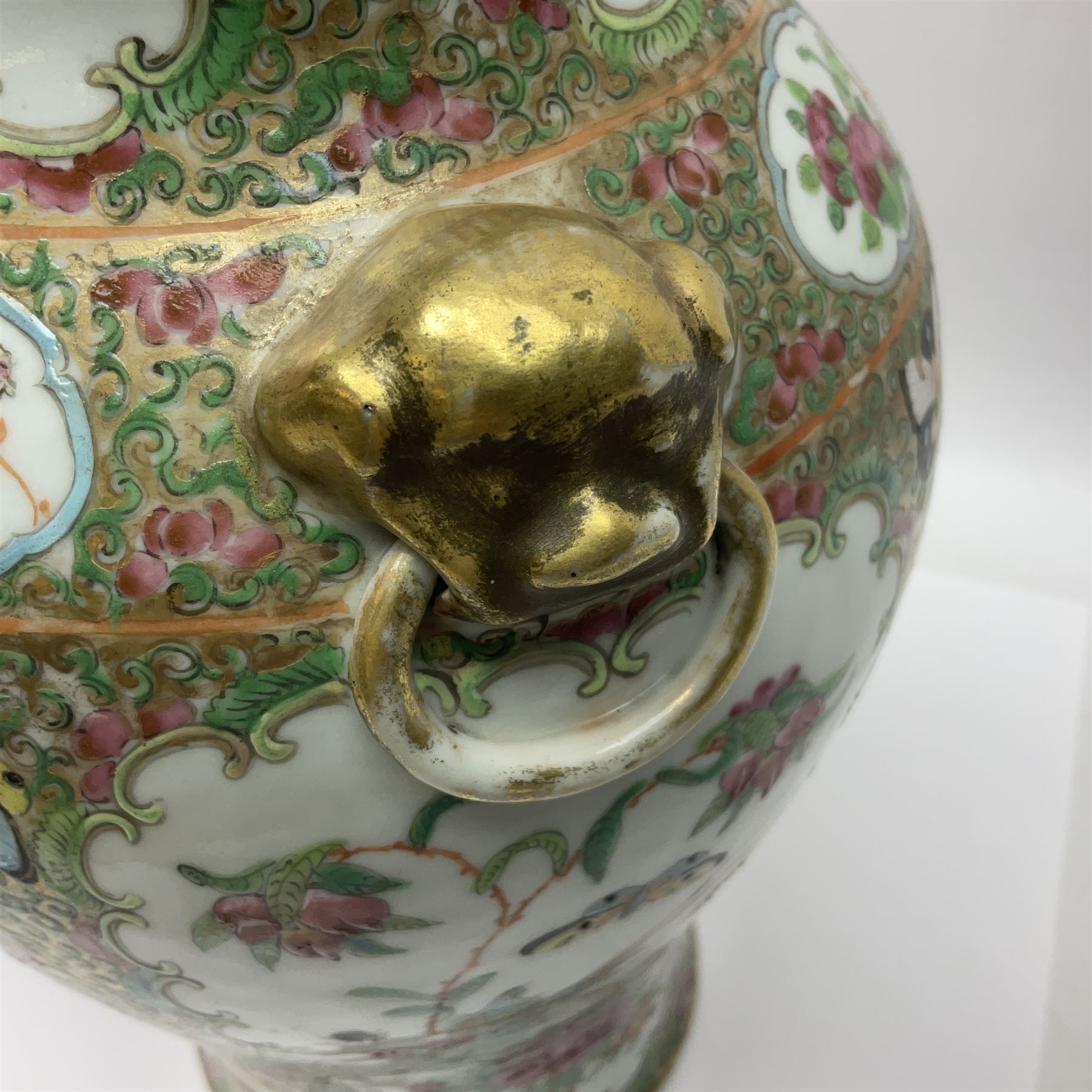 Pair of 19th century Chinese Famille Rose vases and covers, each of baluster form with twin gilt lion mask ring handles to shoulders, the flattened domed covers with gilt temple lion finials, each decorated with alternating reserves of bijin and attendants, and birds and butterflies amongst blossoming peonies, against a gilt ground profusely decorated with stylised scrolls, H32.5cm