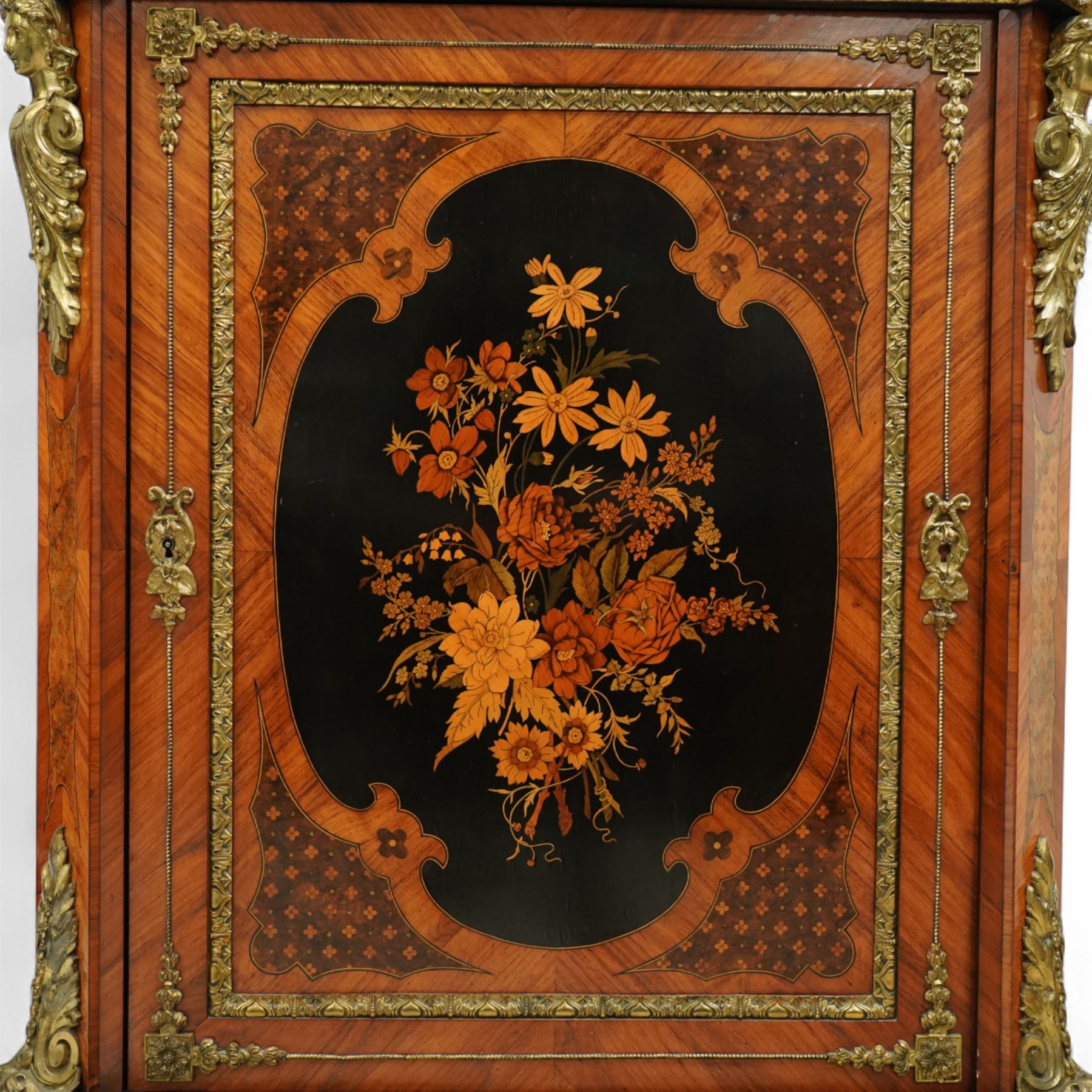 Late Victorian floral marquetry and ormolu mounted side cabinet, with white marble top above a frieze of floral inlay, single cupboard door revealing a shelved interior, with central floral bouquet panel within gilt-bronze border, flanked by gilt metal mounts of female masks and scrolls, on shaped plinth base