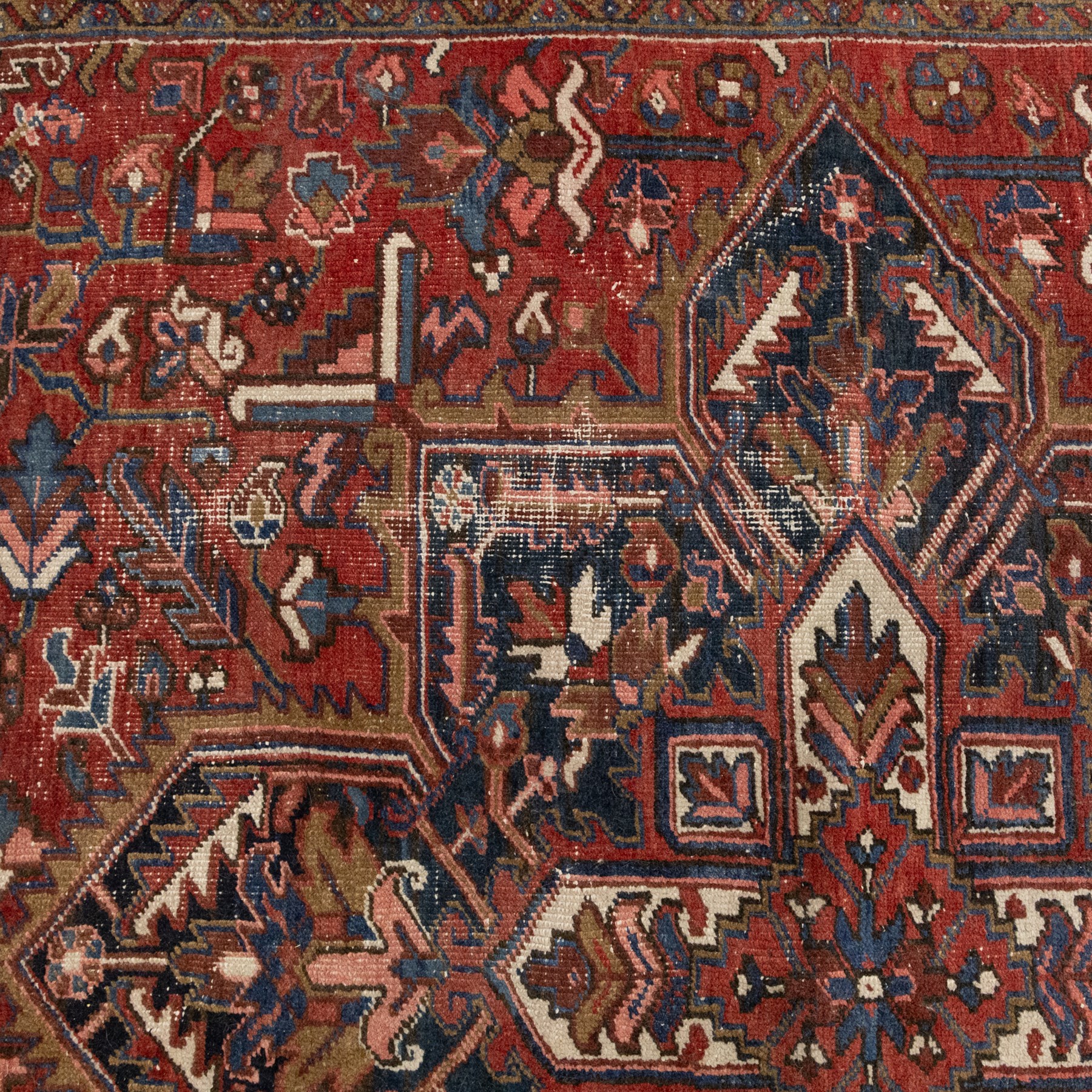 Persian Heriz carpet, red ground with large central geometric medallion, angular flowering branches and stylised foliate decoration, within a broad dark blue floral border and narrow guard stripes