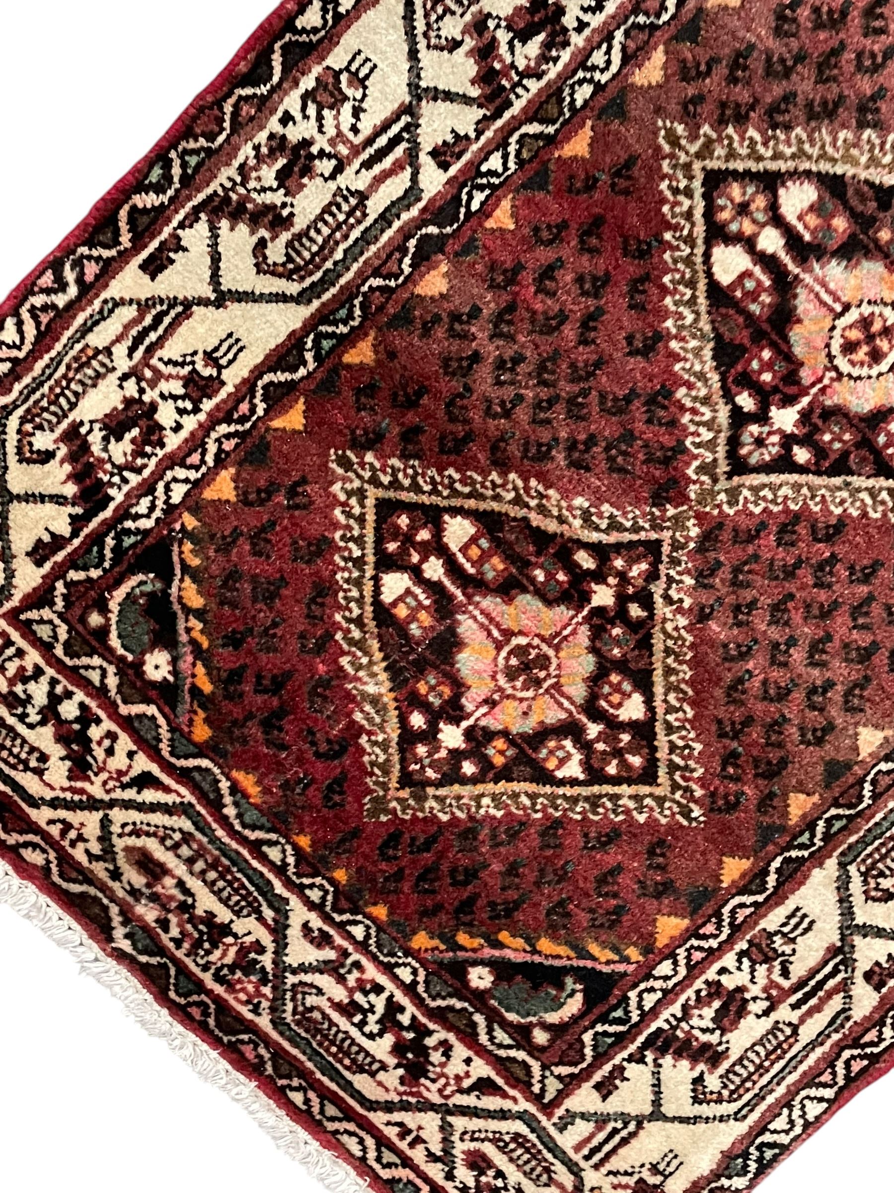 Persian Baluch red ground runner, seven lozenge medallions each decorated with stylised floral motifs, ivory border decorated with trailing pattern and Boteh motifs, within geometric guard stripes 