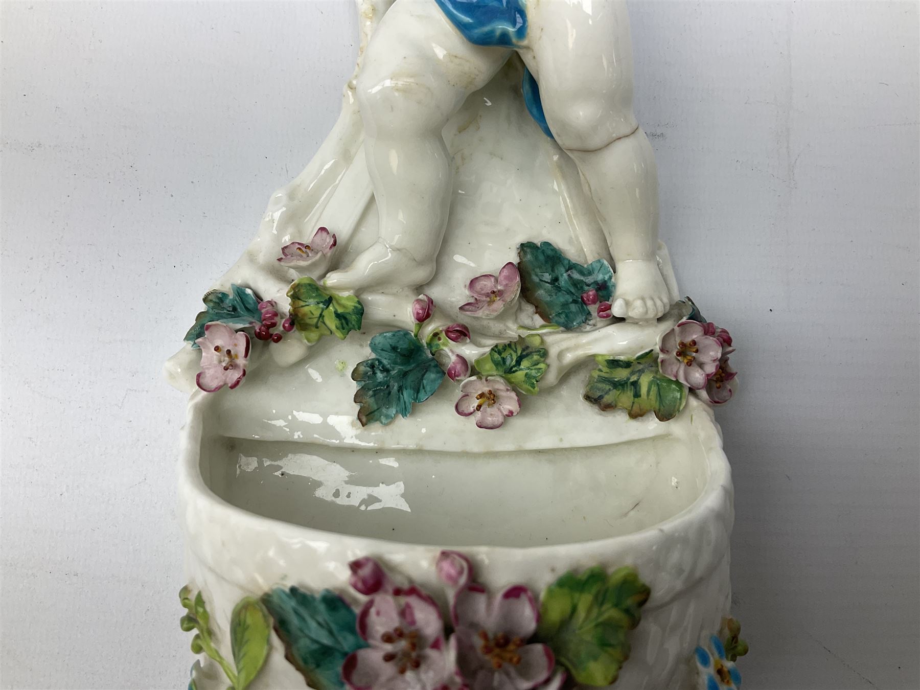 Victorian wall pocket by Moore Brothers retailed by T.Goode modelled as a semi nude white glaze cherub with turquoise ribbon, with encrusted floral decoration, the reverse stamped ‘T.Goode & Co.’, H32cm