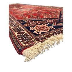 Persian Qashqai crimson ground runner, the central field decorated with three large geometric medallions with intricate angular and floral motifs, the indigo spandrels with complementary geometric designs, bordered by an ivory band with repeating floral patterns and angular vines
