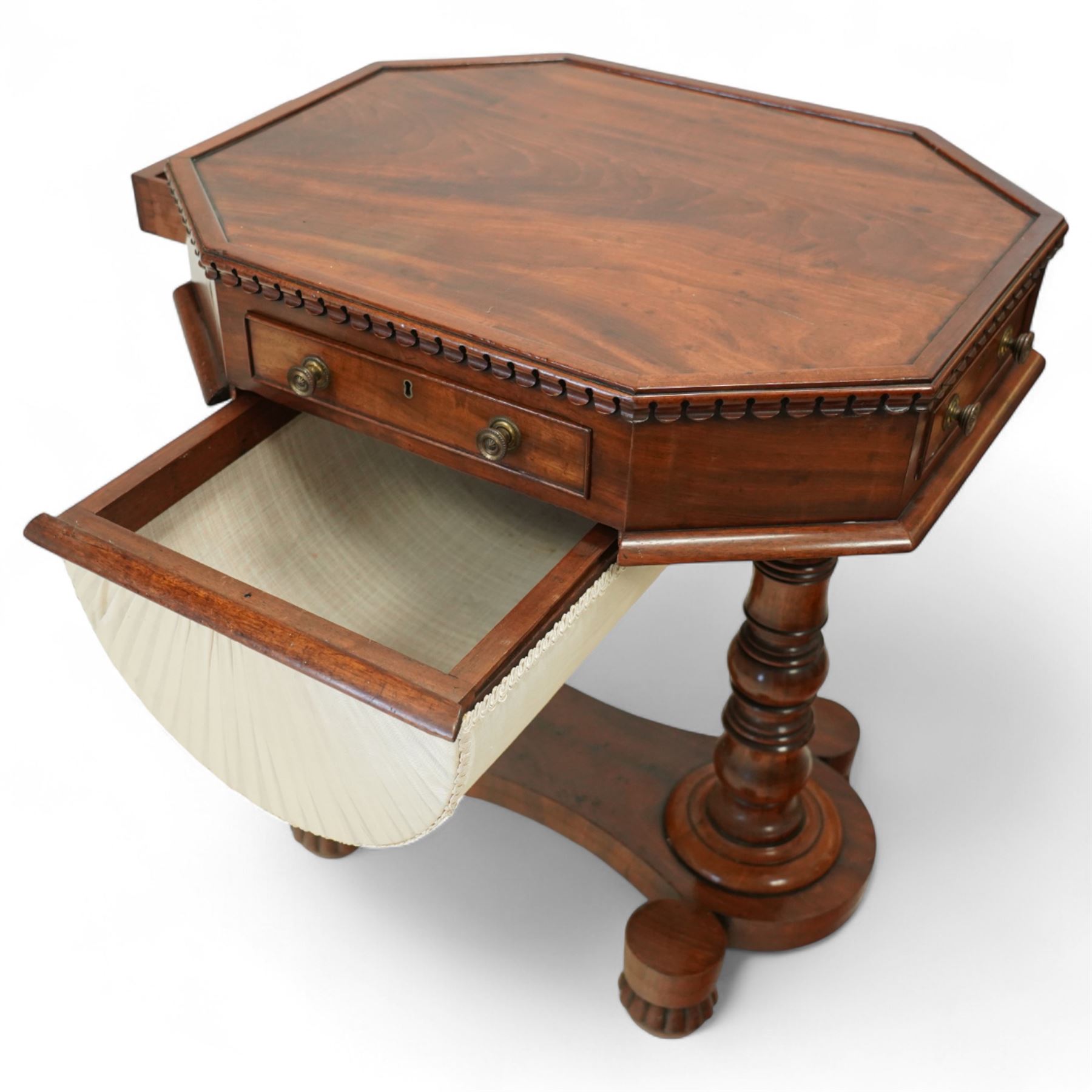 William IV mahogany work table, the octagonal top with ebony line inlay and dentil moulded edge, fitted with four small drawers to the frieze, above a silk-pleated sliding work basket, all raised on a turned column supports and shaped platform base with rounded feet, circa 1835