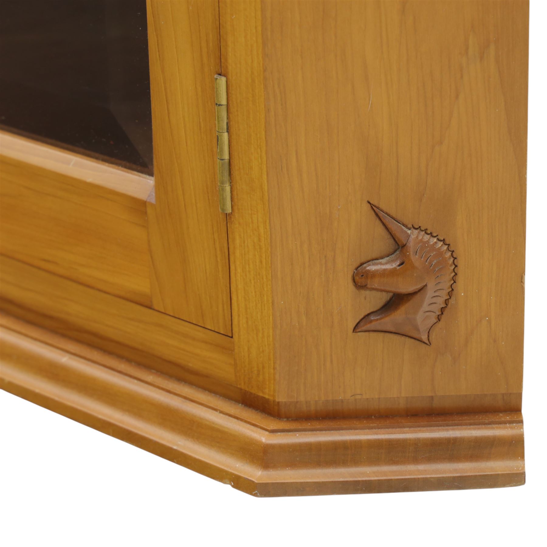 Unicornman - glazed oak corner cabinet, the triangular top with moulded cornice above a bevelled glass door, enclosing two fixed shelves, the canted front corner carved with Unicorn motif, by Geoff Gell of Coxwold