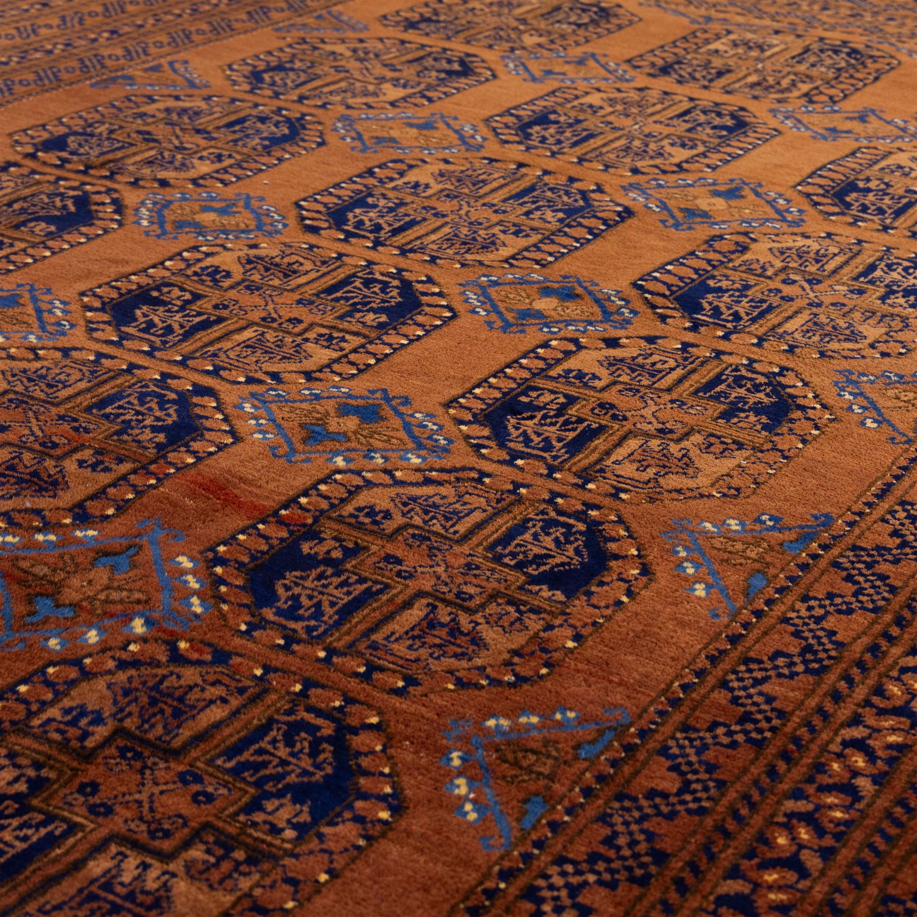 Pakistani Bokhara hand-knotted carpet, camel field decorated with rows of large tekke style octagonal guls enclosing stylized geometric motifs, interspersed with small stepped diamond devices within multiple geometric borders, with fringe ends 