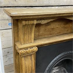 20th century fireplace, oak surround with moulded and scroll carved upright pilasters, with Victorian style cast iron inset and grate, the aperture decorated with flower head motifs