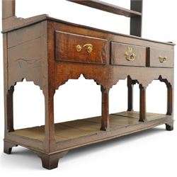 18th century Georgian oak dresser base with plate rack, the three-tier plate rack with shaped frieze, the base with rectangular top with raised back fitted with five spice drawers, over three drawers with brass swan neck handles, raised on six square chamfered supports united by undertier 
