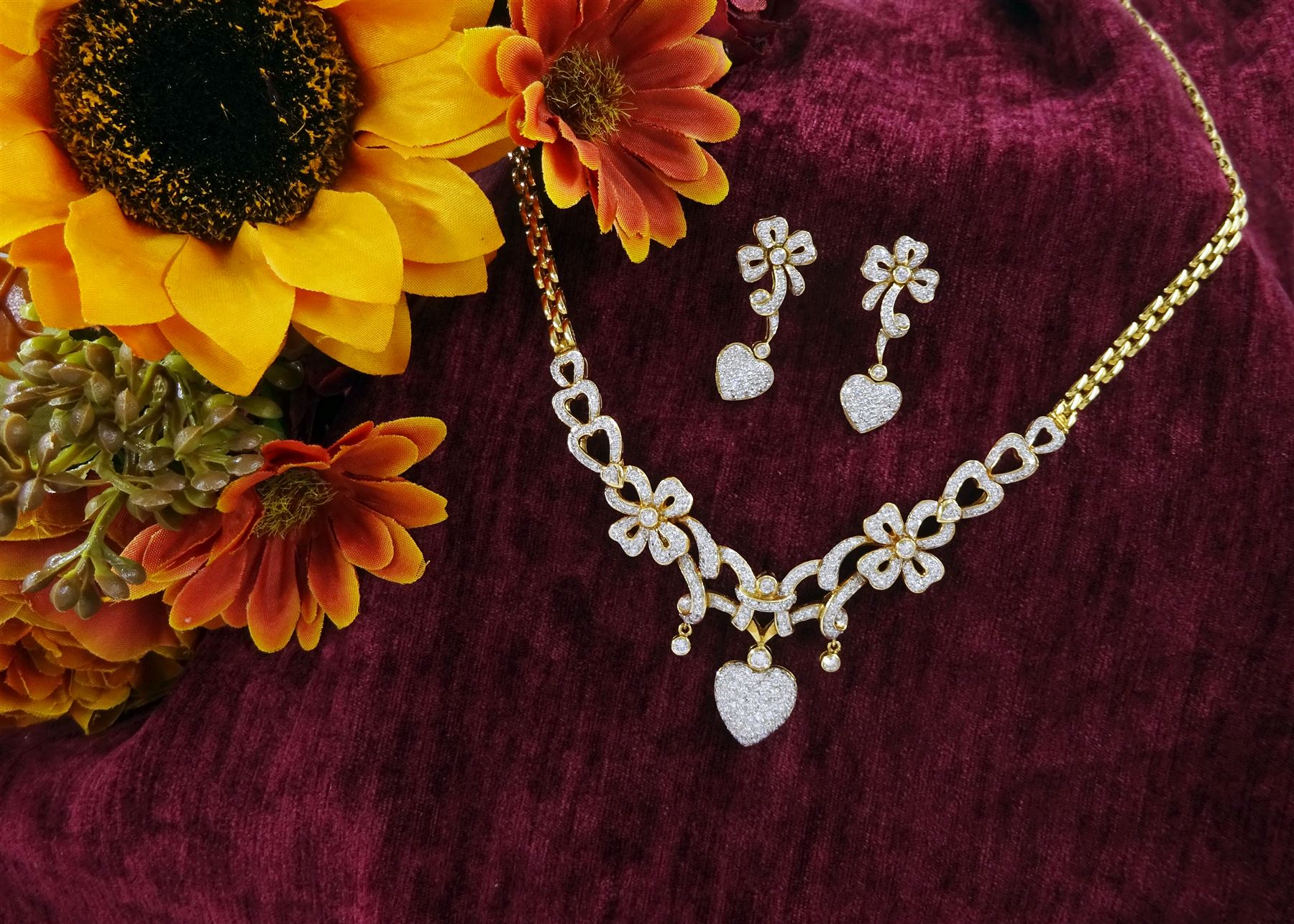 18ct gold diamond heart and bow necklace, the central panel set with round brilliant cut diamond hearts, bows and ribbons, suspending a further pave set diamond heart pendant, to a brink link chain necklace, stamped 750