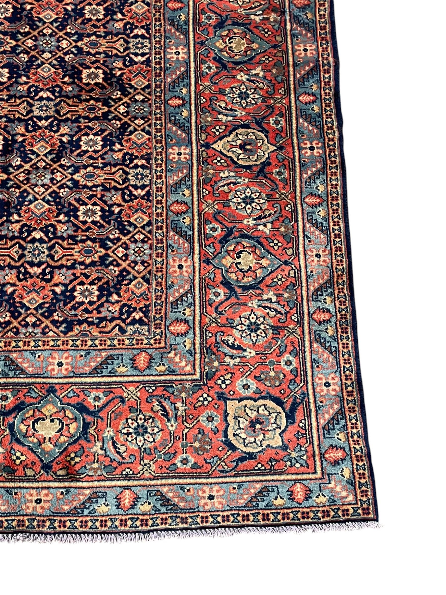Persian Heratti indigo ground carpet, the busy field decorated with repeating floral pattern Heratti motifs, scrolling leafy branches and palmettes to the crimson ground border, within foliate pattern guard stripes 