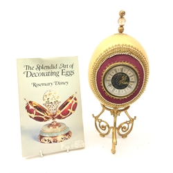  Ostrich egg mantle clock with beaded and gilt thread embellishment, on scroll triform base with 'Mercedes' quartz movement H31cm and related book 'The Splendid Art of Decorating Eggs' by Rosemary Disney (2)   