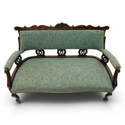 Edwardian mahogany framed sofa, shaped cresting rail with scroll terminals and carved foliate pediment, upholstered back and swept arms in green foliate fabric, pierced splat supports, serpentine front seat rail, on cabriole supports terminating in castors