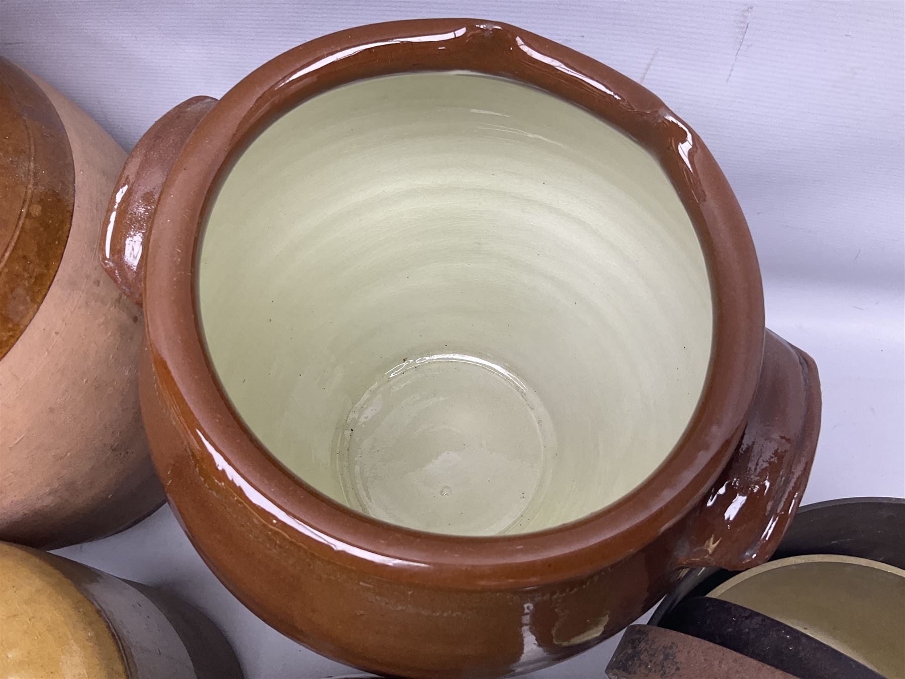 Quantity of stoneware flagons, to include Skipton, Clitheroe and Hellifield related examples, four salt glazed bottles, large cylindrical stoneware jar, large twin handled jar and vase, together with two brass jam pans, tallest H35cm