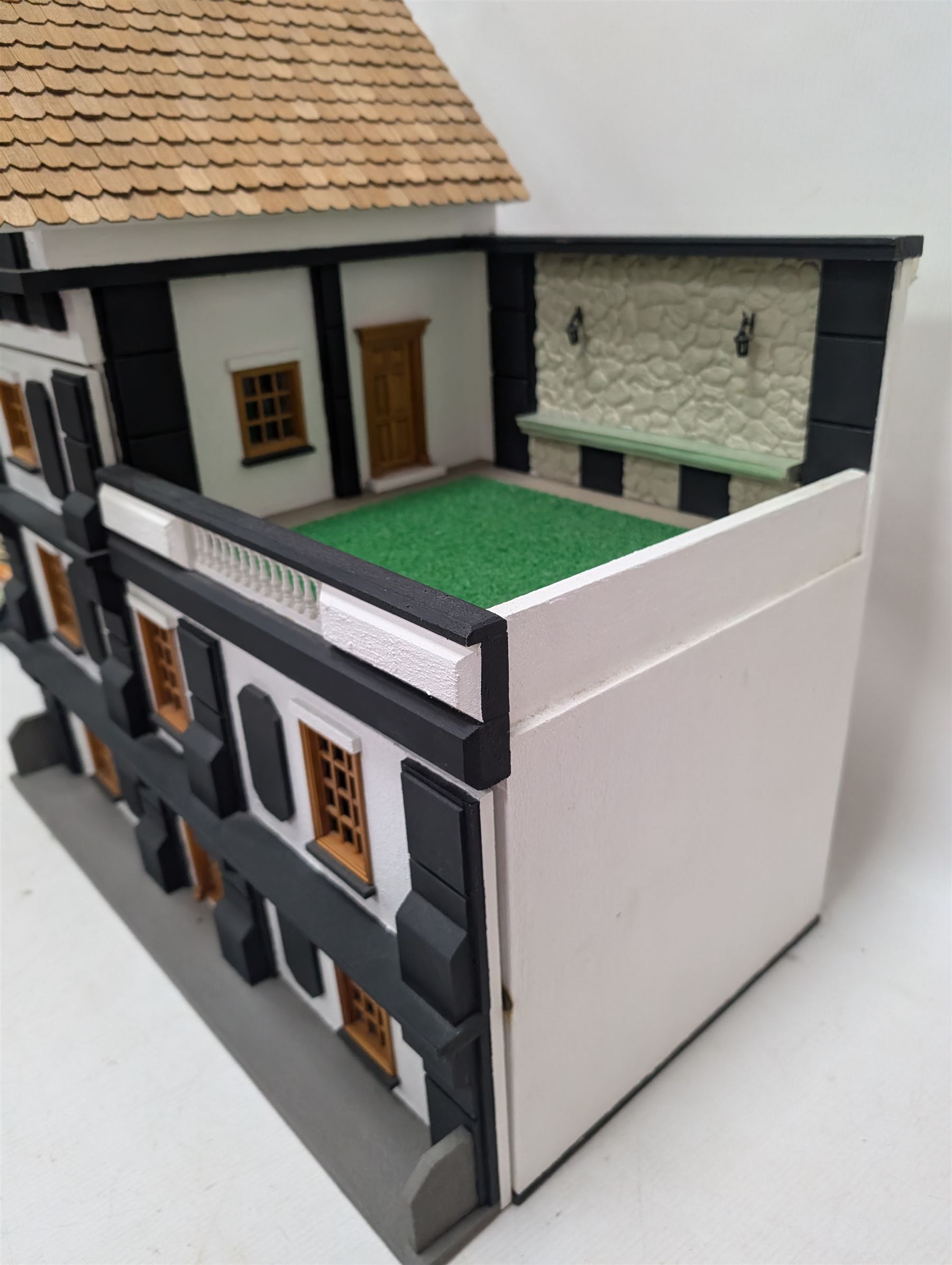 1:24 scale four-storey tudor-style dolls house, with black and white exterior, balcony garden, glazed panelled windows and wooden shingle roof, with decorated interior and wired fireplaces and lighting, H65cm, W58cm, D31cm, 