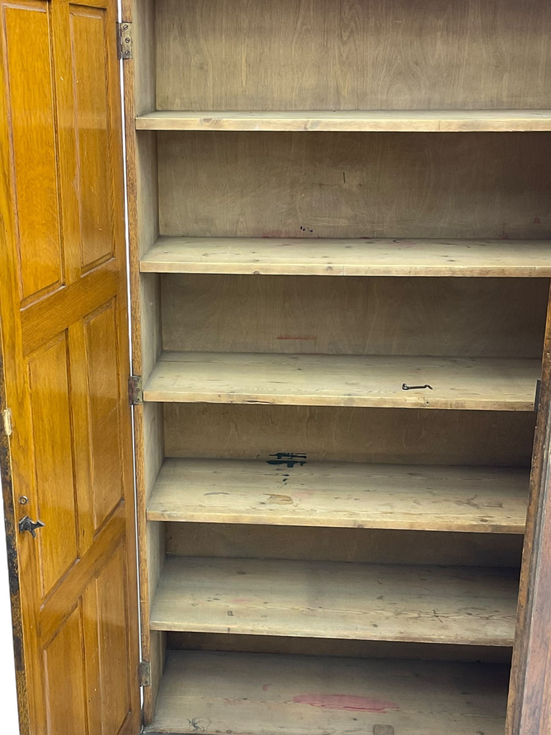 The North of England School Furnishing Company Limited Darlington - early 20th century oak school cupboard, projecting moulded cornice over two panelled doors, fitted with shelves, on chamfered plinth base 