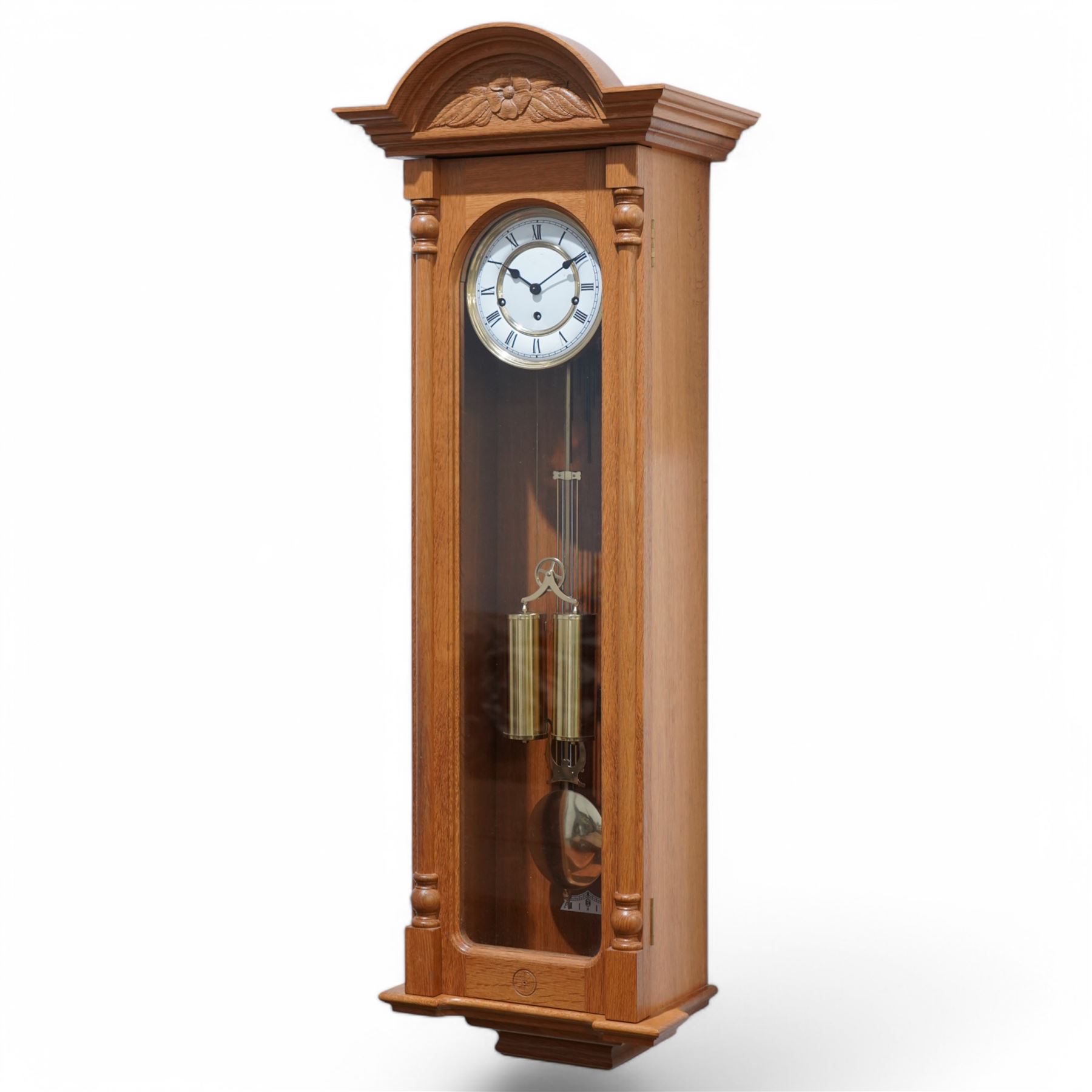 Carthouse - 20th century oak cased 8-day wall clock with a break arch pediment and carved tympanum,  fully glazed case door with full length pilasters, visible gridiron pendulum, beat plate and twin brass cased weights suspended on a single bridge pulley, enamel two part dial with Roman numerals, minute track and spade hands, German, Joseph Kieninger RWS three train movement with a weight  driven going train and spring driven strike and chiming trains, chiming the quarters and striking the hours on gong rods. With weights, pendulum and key.  