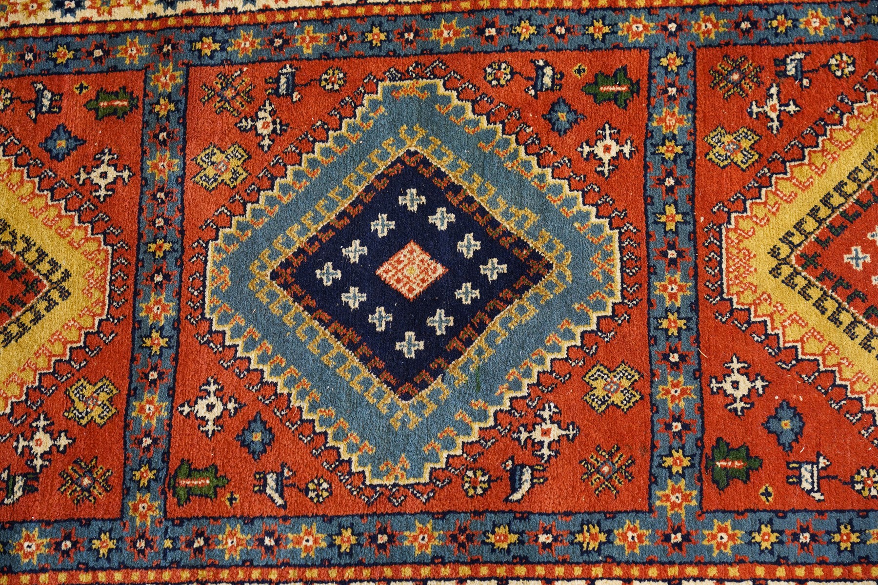 Caucasian Kazak vermillion ground rug, the sectioned field decorated with three geometric lozenge medallions surrounded by stylised plant and animal motifs, the multiple guard bands with repeating geometric design