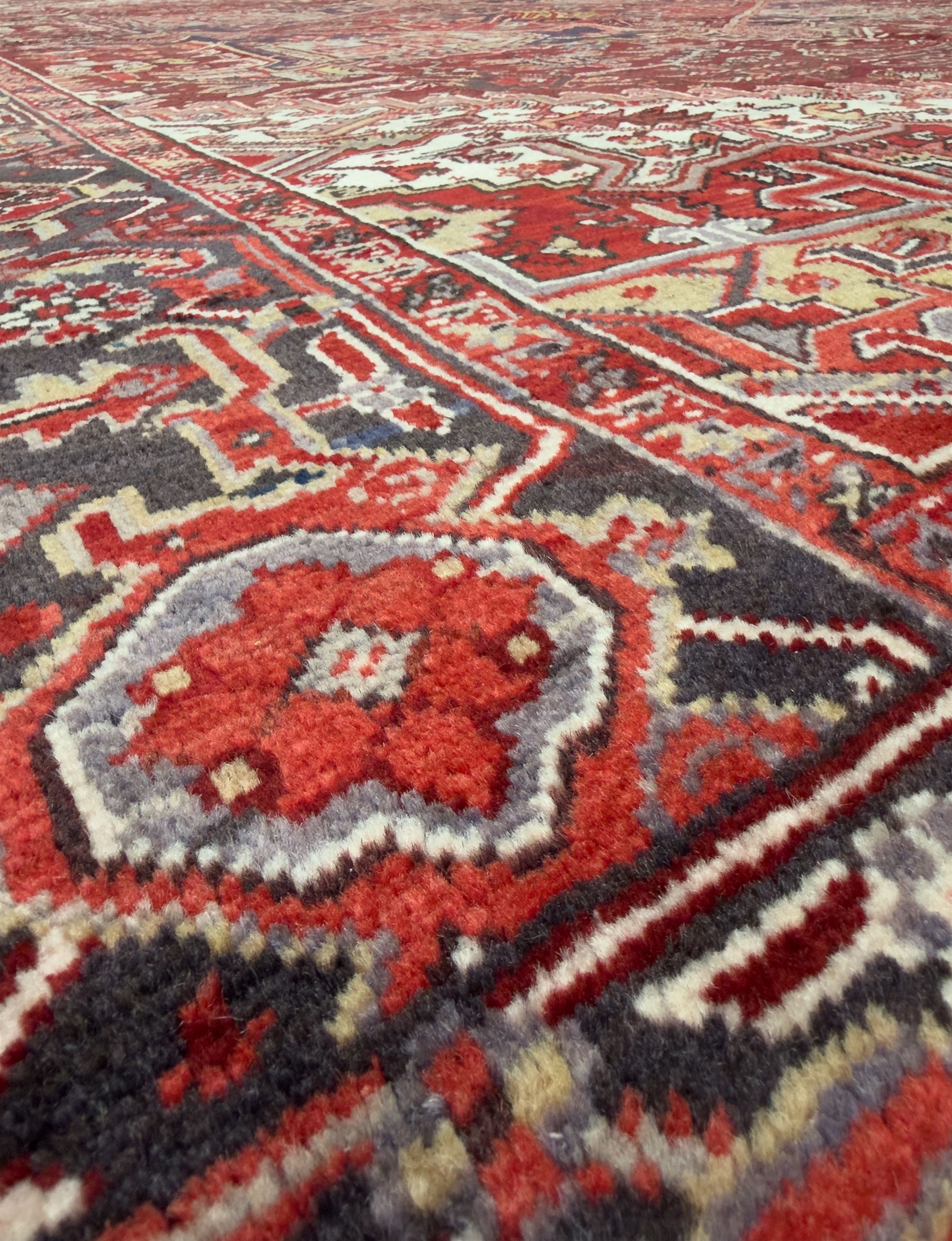 Northwestern Persian Heriz carpet, the madder red field centred by a large octofoil medallion with serrated edge, flanked by ivory stepped spandrels and geometric floral motifs in indigo, ochre and sky blue, enclosed by a navy border of rosettes and angular vines, from the region of Heriz