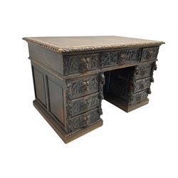 Late 19th century Gothic revival carved oak twin pedestal desk, rectangular top with inset writing surface and carved edges, central frieze drawer flanked by eight drawers, all with green man carved handles and extending trailing foliage, carvings of pineapple and lion mask corbels, the pedestals with panelled sides and back, on plinth bases