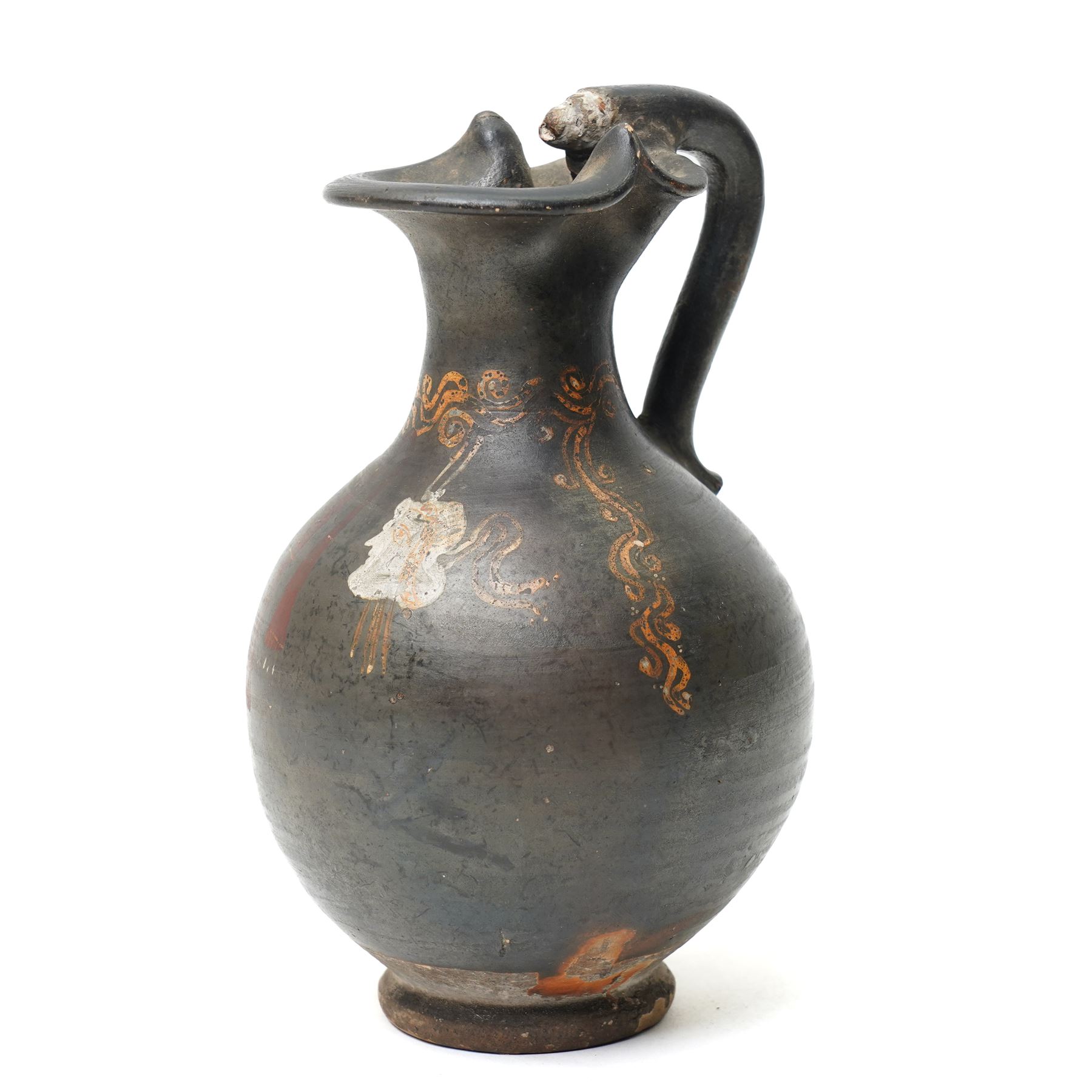 South Italian Gnathian terracotta oinochoe (jug) Apulian or Campanian (Late 4th century BC c.325-300 BC) of elegant ovoid form with trefoil mouth and single strap handle, the handle terminating in a stylised serpentine motif merging into the pouring lip, the vessel covered in a black gloss slip and decorated in added red, white and yellow with a theatrical mask, fillets and scrolling Dionysiac vine motifs, H19cm 
Notes: Gnathian ware takes its name from Egnathia in Apulia and is characterised by a black-gloss ground with added-colour decoration; the theatrical mask, fillets and vine scrolls relate to Dionysiac imagery associated with the symposium and theatre in South Italian Greek culture of the late fourth century BC. A very similar oinochoe is held in the The Metropolitan Museum of Art, object number 76.12.8