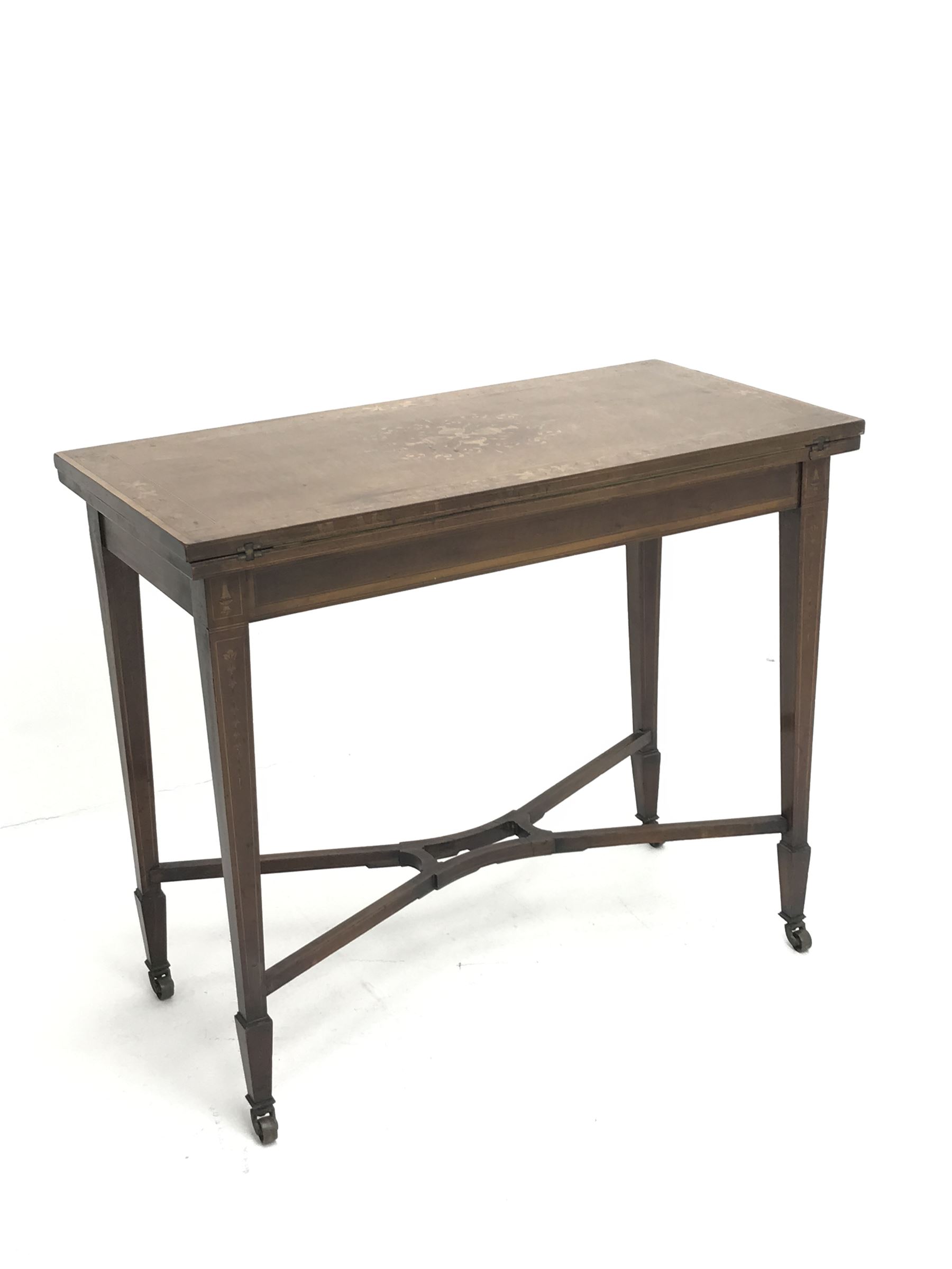 Edwardian walnut and mahogany Sheraton revival card table, rectangular top cross banded and inlaid with scrolling foliage, the central inlay with four urns and trailing leafage, swivel fold over action revealing storage well and baize lined interior, husk inlaid square tapering supports with spade feet, shaped and pierced x-framed stretcher, brass castors