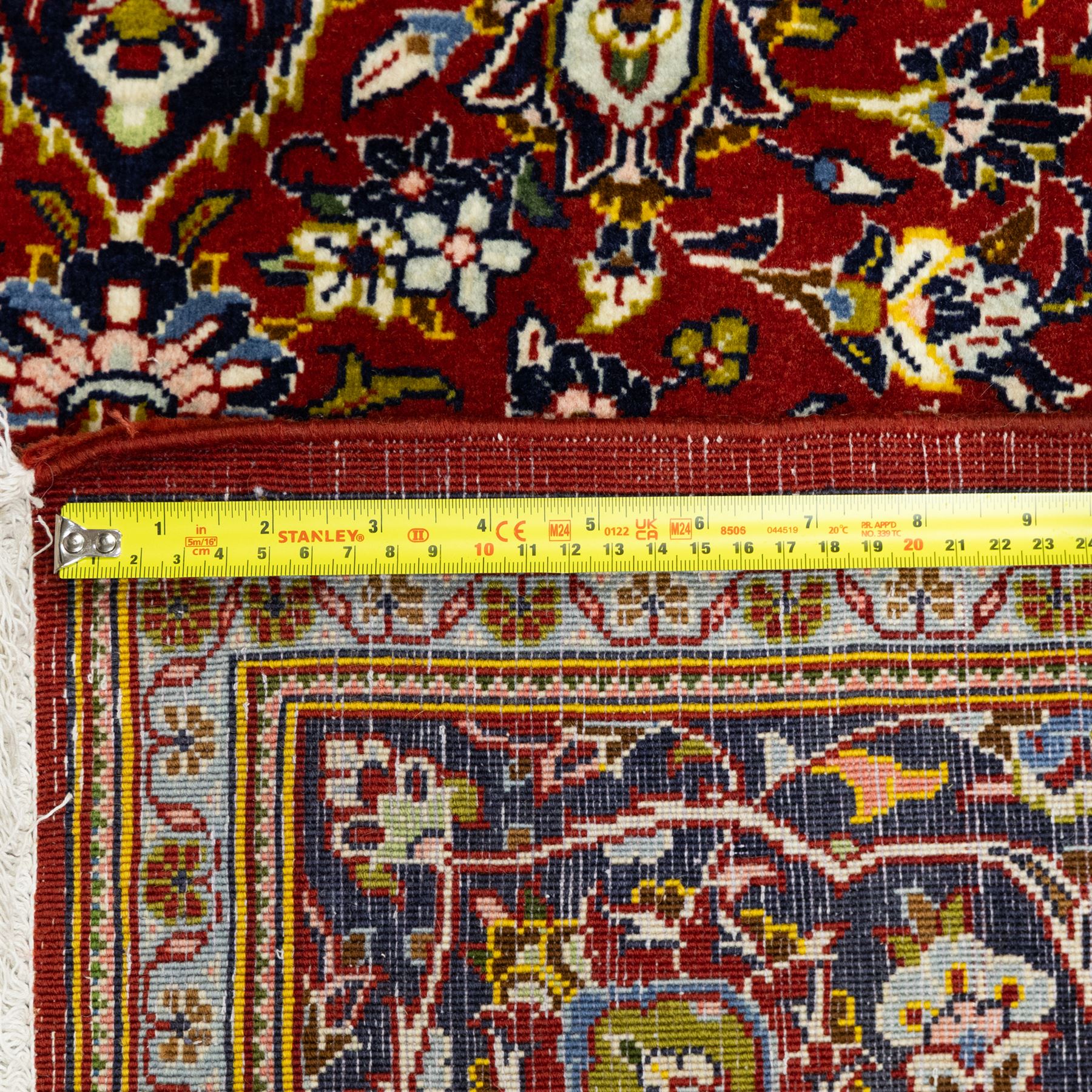 Central Persian Kashan hand-knotted carpet, crimson ground, with a central ivory shaped floral medallion with pendants, surrounded by dense scrolling foliate and floral motifs incorporating rosettes, palmettes and delicate vine work, enclosed by ivory spandrels and a dark navy border with repeating palmettes and meandering vines, flanked by floral guard stripes, with cotton fringes