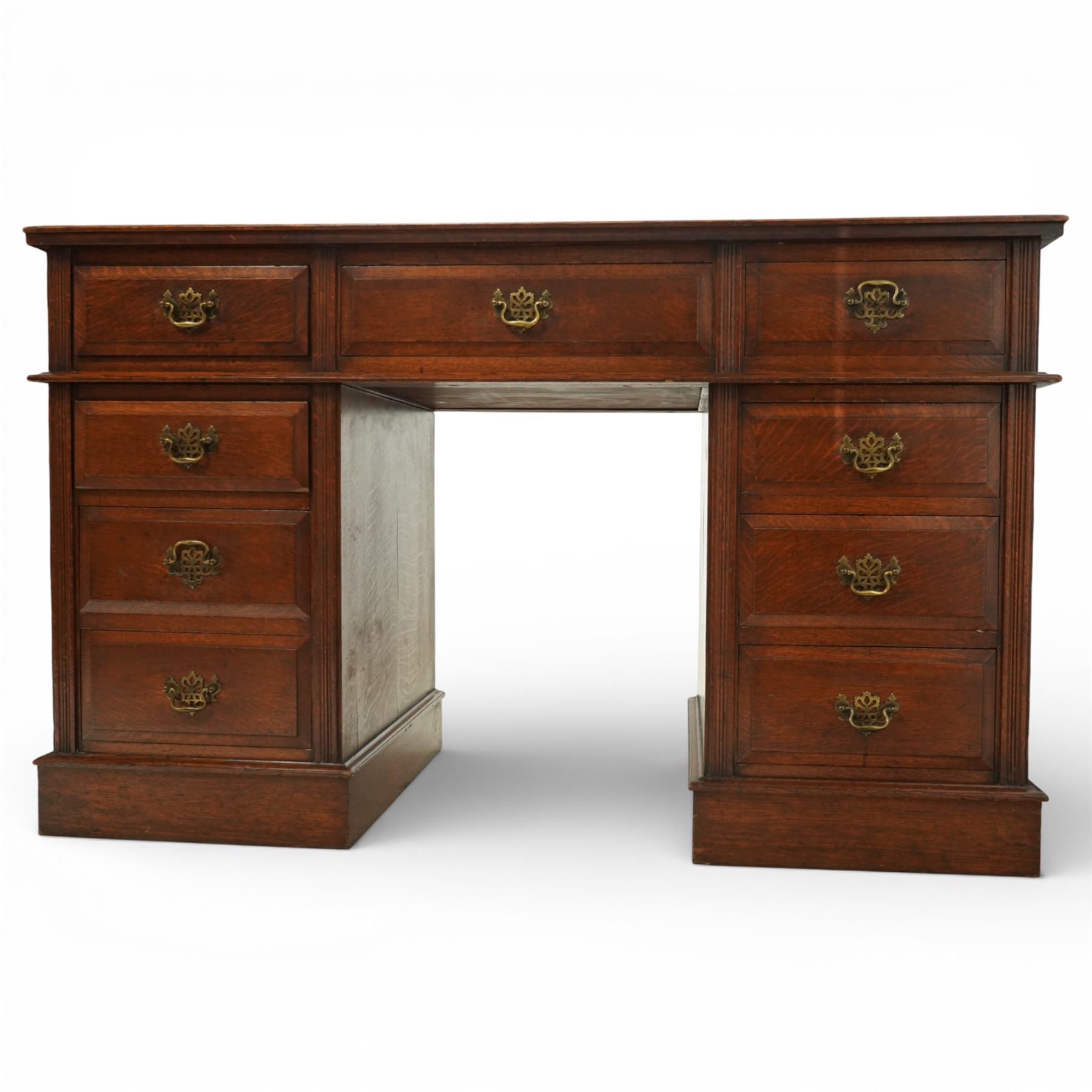 Late Victorian oak nine drawer desk, the rectangular top inset with a tooled leather writing surface bordered in gilt, above three frieze drawers and two pedestal cupboards each fitted with three graduated drawers, all with brass swan neck handles, raised on plinth bases