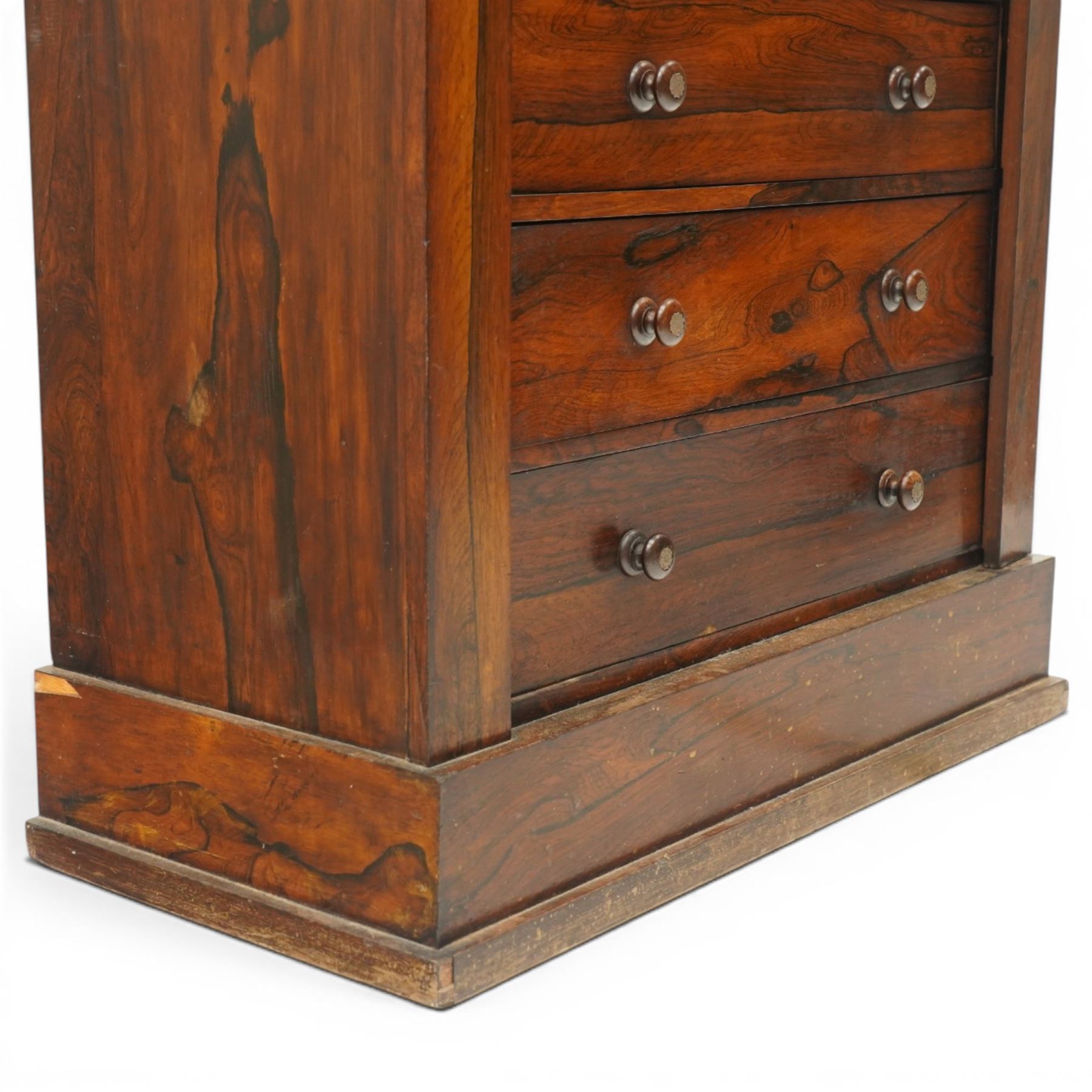 Victorian rosewood Wellington secretaire chest, the projecting stepped cornice over a banded frieze with moulded rosette mounts, single drawer over a secretaire fall-front opening to reveal a maple lined interior with assorted pigeonholes and correspondence drawers, over a lappet carved lower edge with four graduating drawers below, each with turned pull handles, flanked by hinged lock to the right and plain stile to the left surmounted by reeded corbels, raised on a skirted base