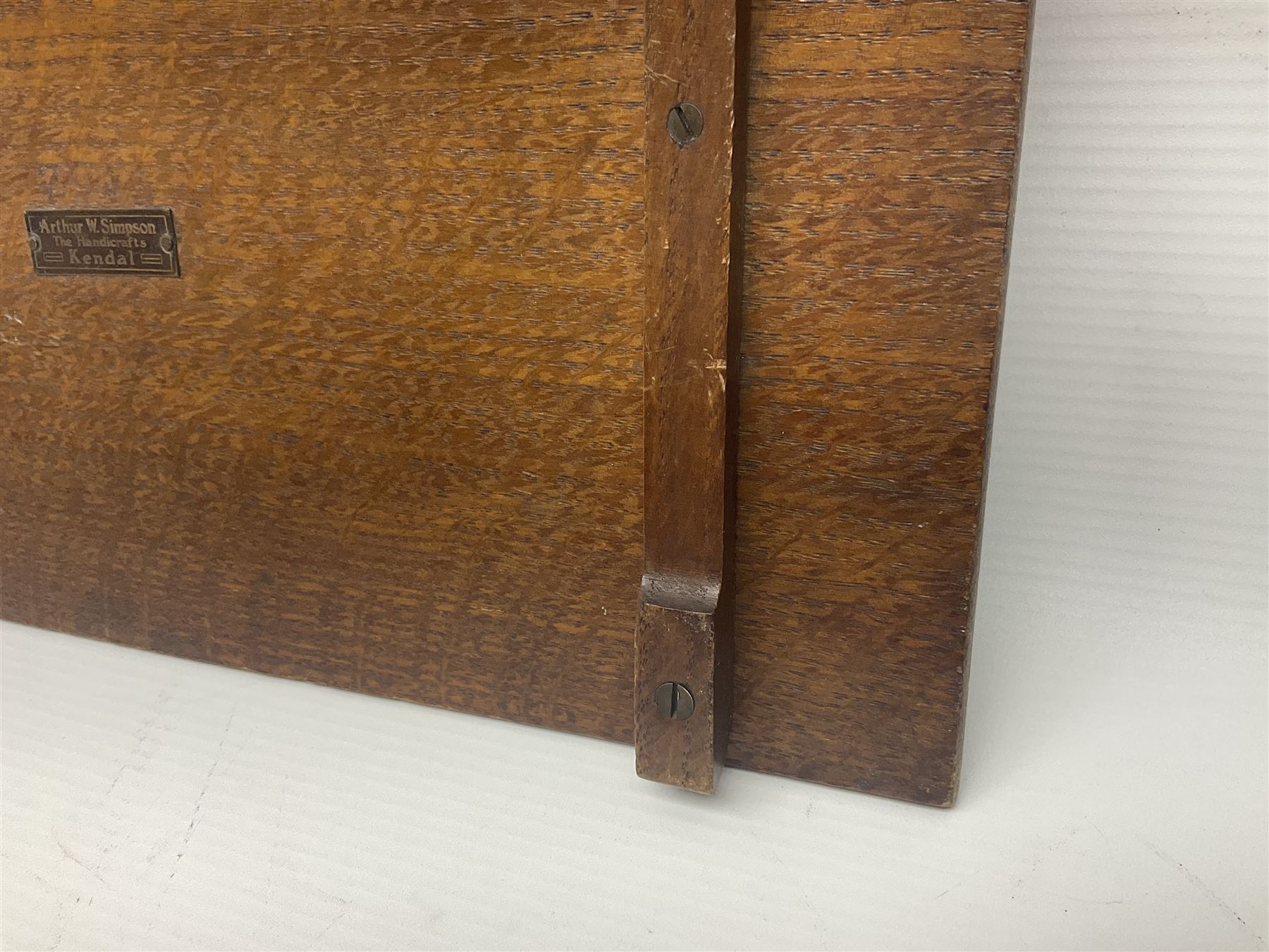 Arts and Crafts oak stand by Arthur Simpson of Kendal, of rectangular form with central hammered pewter panel, surrounded by a border with carved foliate corners, upon two bar supports, bearing label detailed 