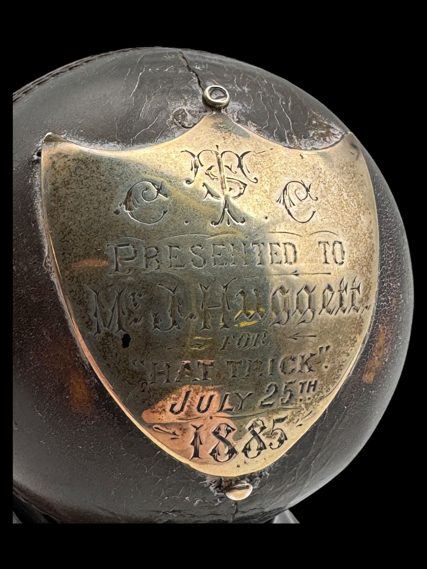 Victorian presentation 'Hat Trick' cricket ball, with applied silver shield cartouche presented to Mr J Hugger 1885, upon ebonised wooden stand