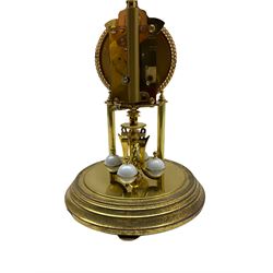 A 20th century Kundo Anniversary 400 Day clock, made by German manufacturer Kieninger & Obergfell, with a gilt brass base and four ball rotary pendulum, white painted dial with gilt three-hour Arabic numerals and batons, with pierced brass hands, open bezel with gilt ropework design, under a glass dome.
No Key. 
