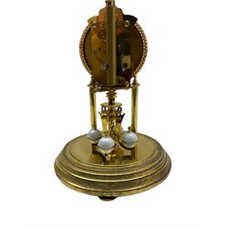 A 20th century Kundo Anniversary 400 Day clock, made by German manufacturer Kieninger & Obergfell, with a gilt brass base and four ball rotary pendulum, white painted dial with gilt three-hour Arabic numerals and batons, with pierced brass hands, open bezel with gilt ropework design, under a glass dome.
No Key. 
