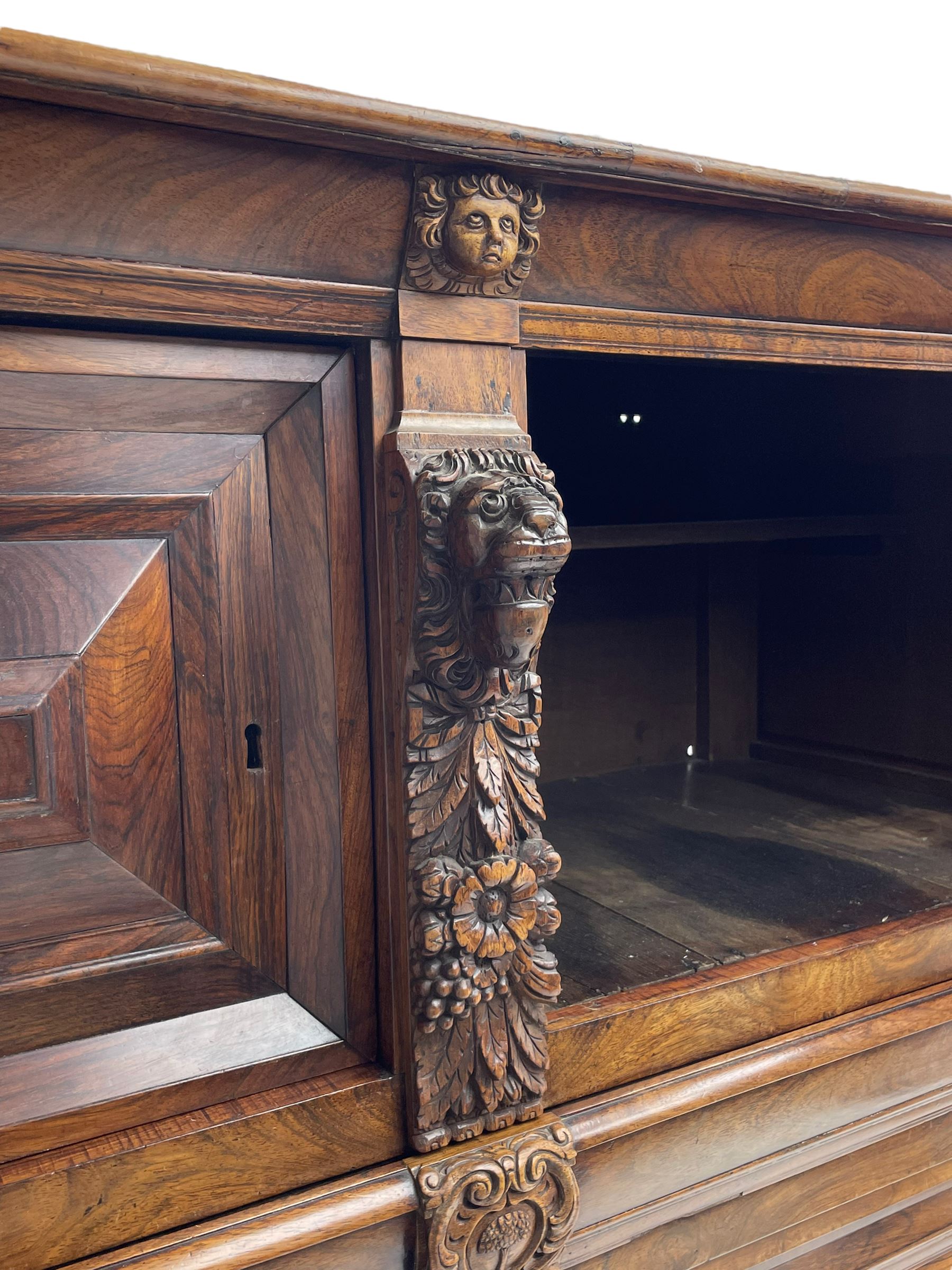 Late 17th century Flemish/Dutch rosewood and oak ‘Zeeuwse Kast’ or cupboard, projecting cornice carved with three putti masks, the uprights carved with lion masks over ribbons, flower heads and foliage, enclosed by four geometric panelled doors, lower central upright carved with flower head over foliate ribbon with bird among foliage, the escutcheon hidden by swivel berry carved cover, interior fitted with shelves, two drawers and shallow hinged cupboard, on two large turned and ebonised feet, circa 1680