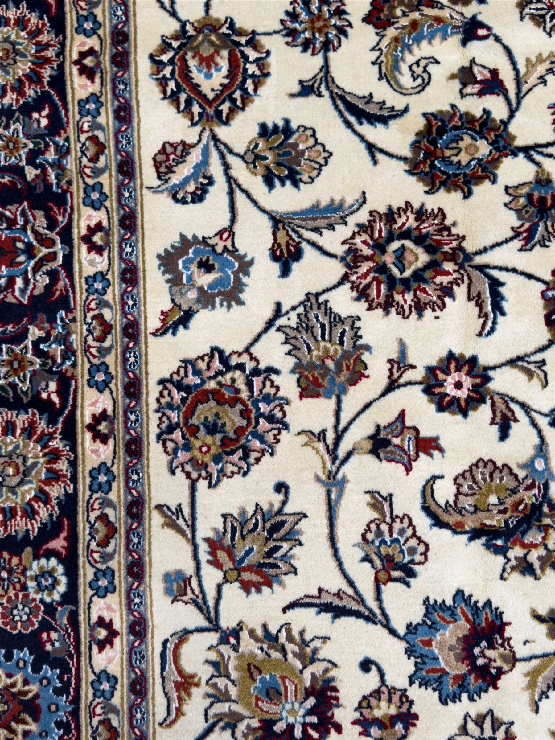 Northeastern Persian Meshed hand-knotted rug, ivory ground with an overall design of scrolling vines, palmettes, and rosettes in an indigo palette, soft blues, and madder, framed by a deep indigo border of lotus palmettes and flowerheads between multiple guard borders, 300cm x 202cm