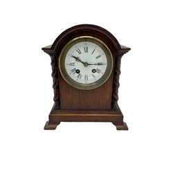 Early 20th century oak cased mantle clock, with a break arch top and barley twist columns,  low plinth raised on oak bracket feet, with a French eight-day movement striking the hours and half-hours on a bell, enamel dial with gothic numerals and steel fleur di Lis hands. With Pendulum.

