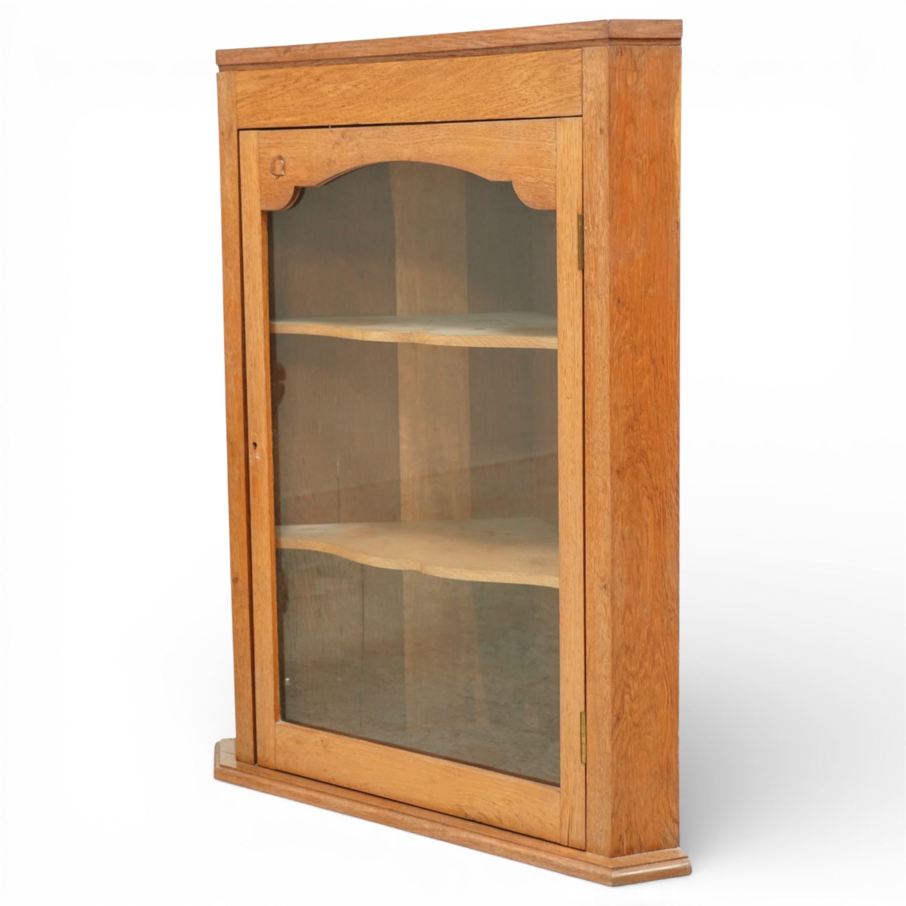 Yorkshire oak corner cabinet, chamfered triangular top above a single glazed door with shaped arched upper rail, enclosing two shaped fixed shelves, plain sides and back, raised on a moulded plinth base, carved with a bell signature