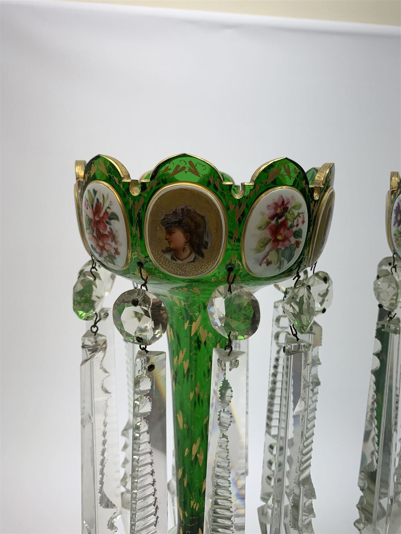 Pair of 19th century Bohemian green glass lustres, the castellated bowls decorated with overlaid panels of flowers and female portraits, upon tapering stems and overlaid spreading feet, heightened throughout with gilt, each supporting ten prismatic drops, H35cm