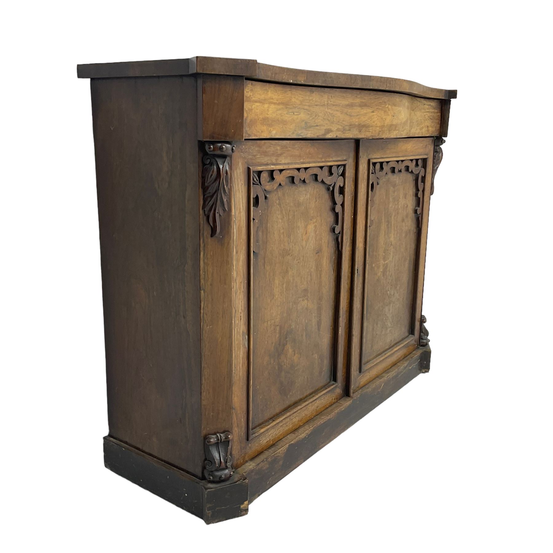 William IV rosewood serpentine chiffonier, fitted with frieze drawer over two panelled cupboard doors with applied C-scroll decoration, flanked by canted uprights with moulded foliate corbels