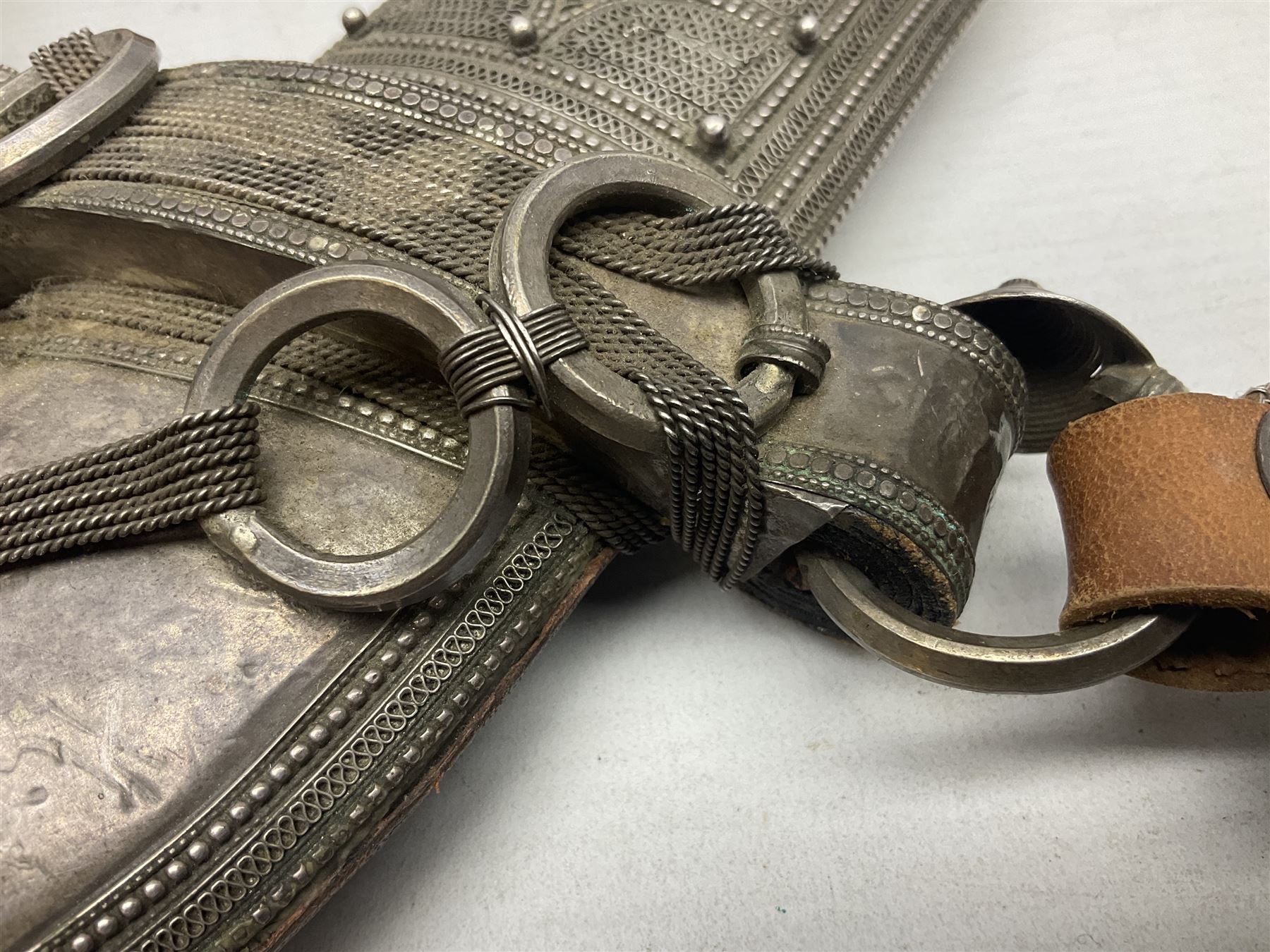 Omani Khanjar dagger, the 19cm curved blade with pronounced medial rib to either side, waisted hilt with dome shaped pommel and silver covered horn grip decorated with filigree bands, floral motifs and beadwork; in an intricately filigree decorated silver and leather scabbard with silver rings woven into the belt mount and fitted with original silver thread-work belt L34cm overall belt length 94cm