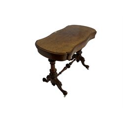 Late 19th century figured walnut card table, shaped hinged swivel top with scrolling satinwood inlay and shaped edge, raised on turned and fluted vasiform supports carved with foliate design united by turned stretcher, on splayed cabriole supports with scroll carving and ceramic castors