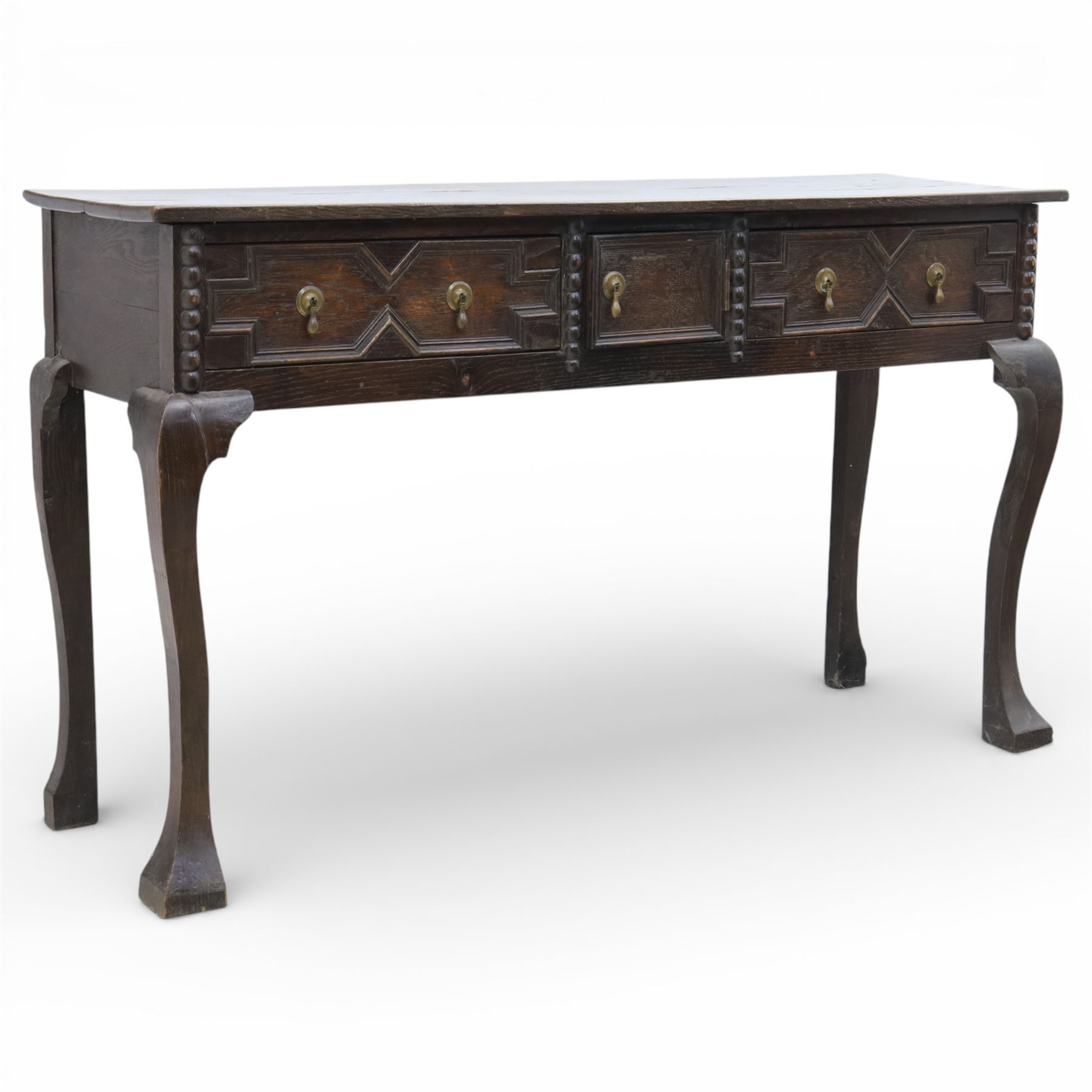 Late 19th century Jacobean revival oak side table, plank top with moulded edge over a central cupboard door and two frieze drawers carved with geometric lozenge motifs and framed by bobbin turned uprights, fitted with brass drop handles, raised on shaped cabriole supports with block feet