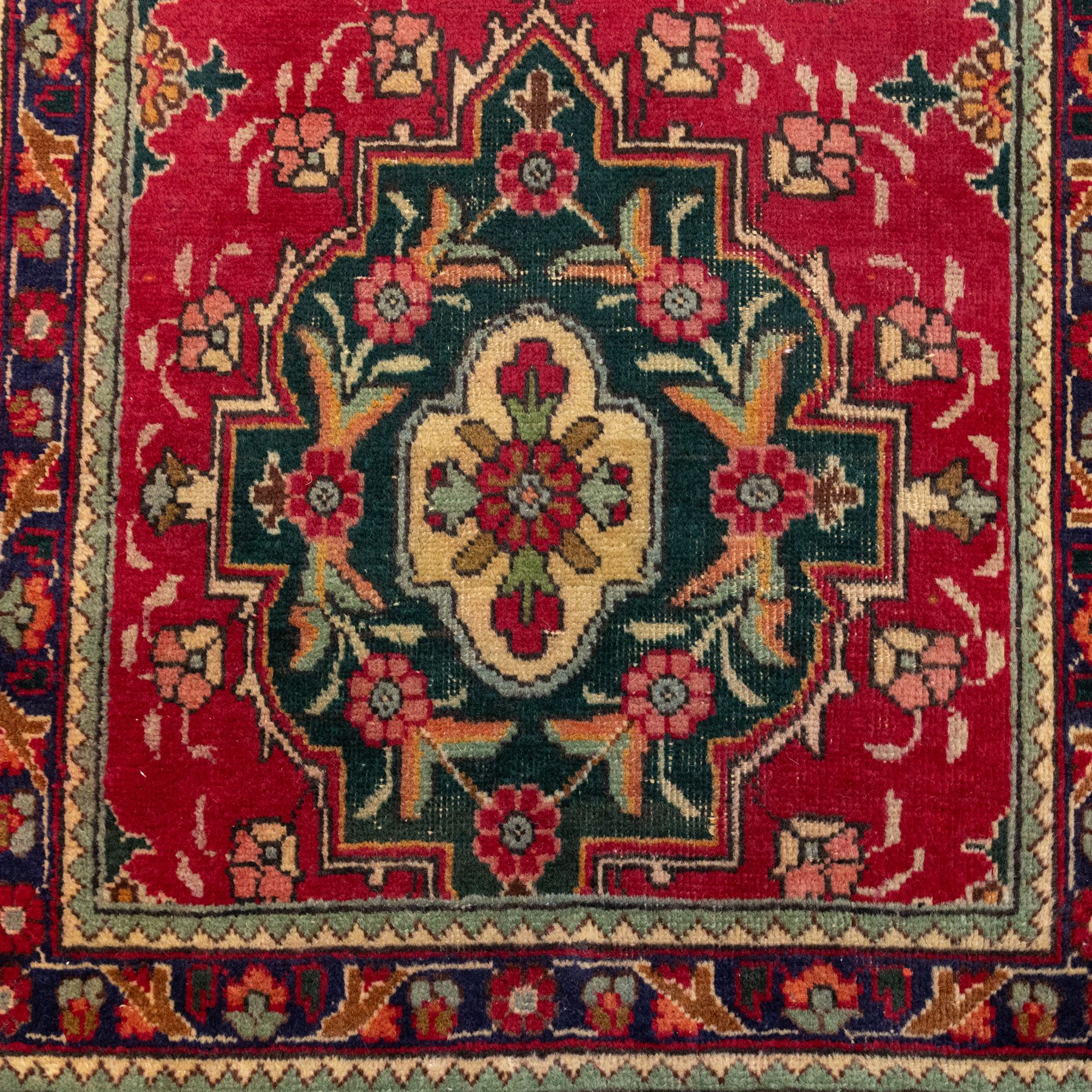 North West Persian Tabriz hand-knotted runner, madder red field with central octagonal medallions of sage green, navy and ivory, ground enclosing a floral rosette and radiating angular vinery, scrolling floral sprays and palmettes either end with shaped pendants principal border on navy ground decorated with a continuous vine-scroll of palmettes and rosettes, flanked by narrow guard borders, with cotton fringe ends 