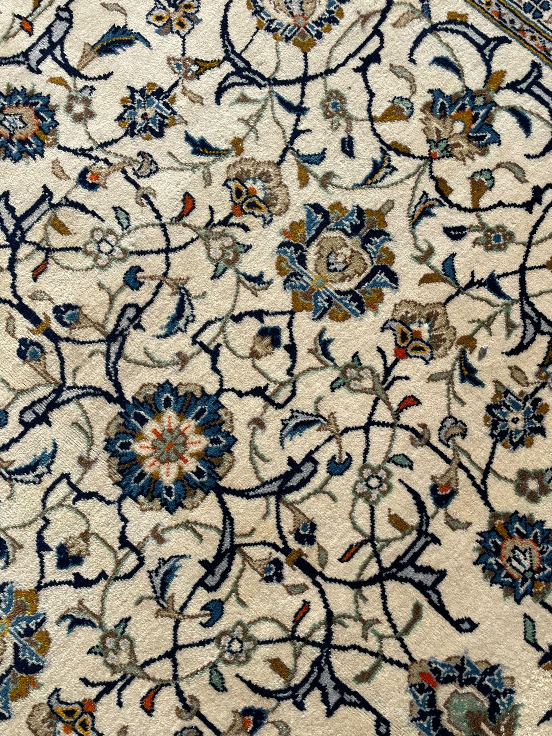 Persian Kashan ivory ground carpet, overall floral design, the field decorated with scrolling and interlaced leafy branches interspersed with palmettes, scrolling border decorated with stylised plant motifs, within floral pattern guard stripes 