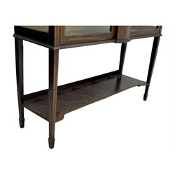 Edwardian mahogany and satinwood crossbanded display cabinet, arched pediment centred by marquetry scrollwork and ribbon decoration, twin glazed doors enclosing a lined a shelved interior, raised on square tapering supports joined by a shaped undertier with diamond parquetry inlay, terminating in spade feet